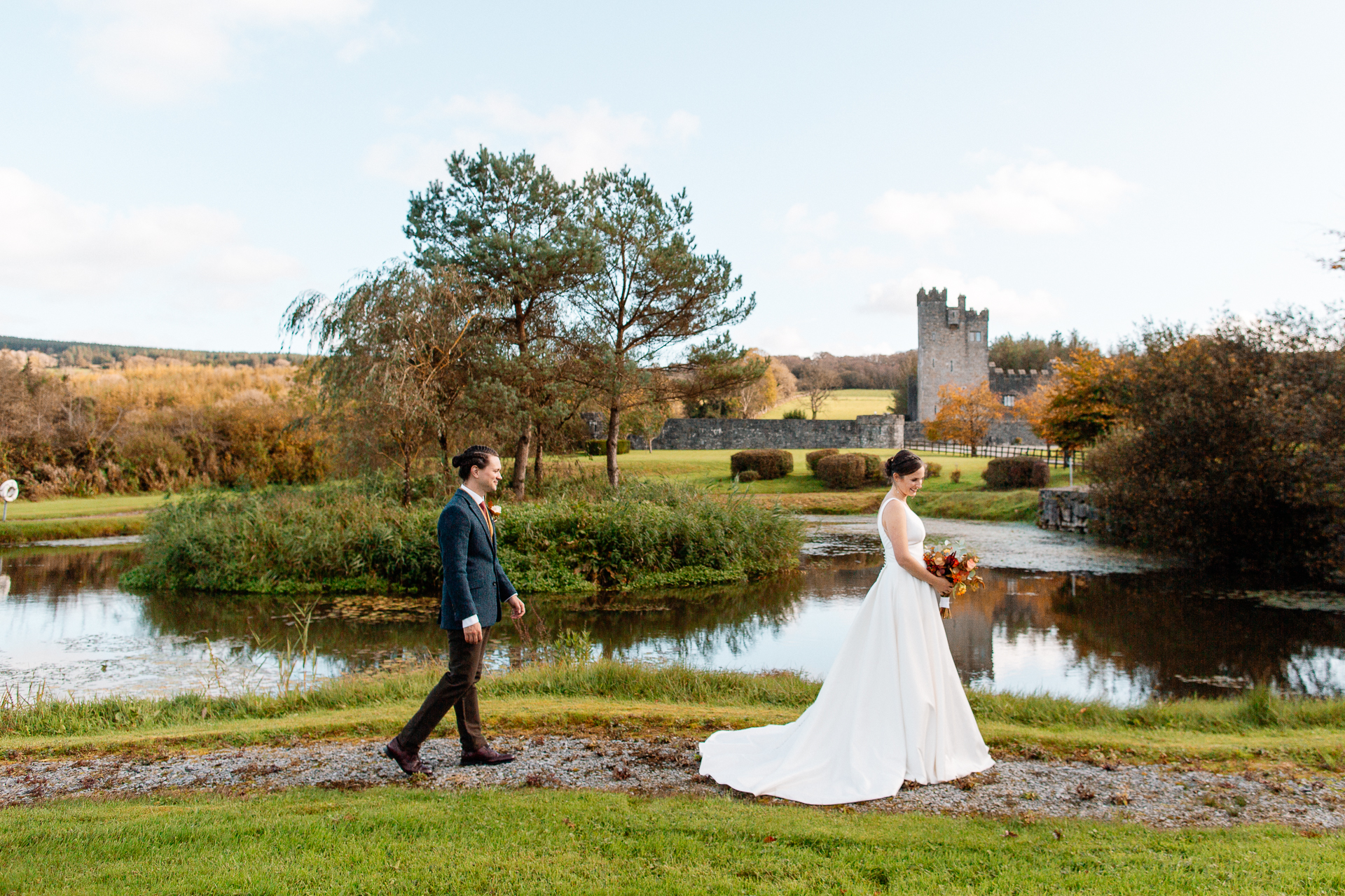 A man and woman walking down a path with a pond and a castle in the background