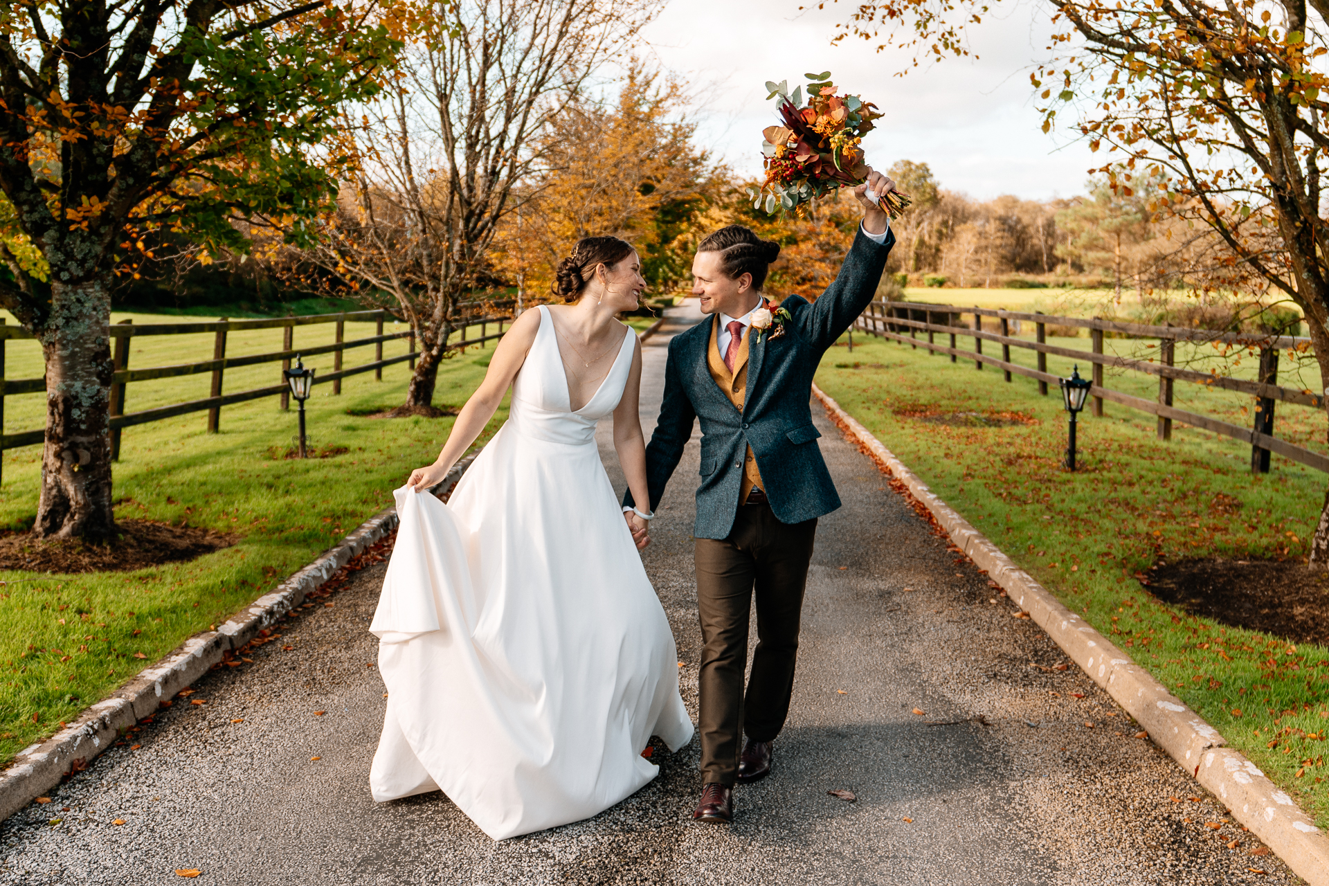 A man and woman holding hands and walking down a path with trees on either side of them