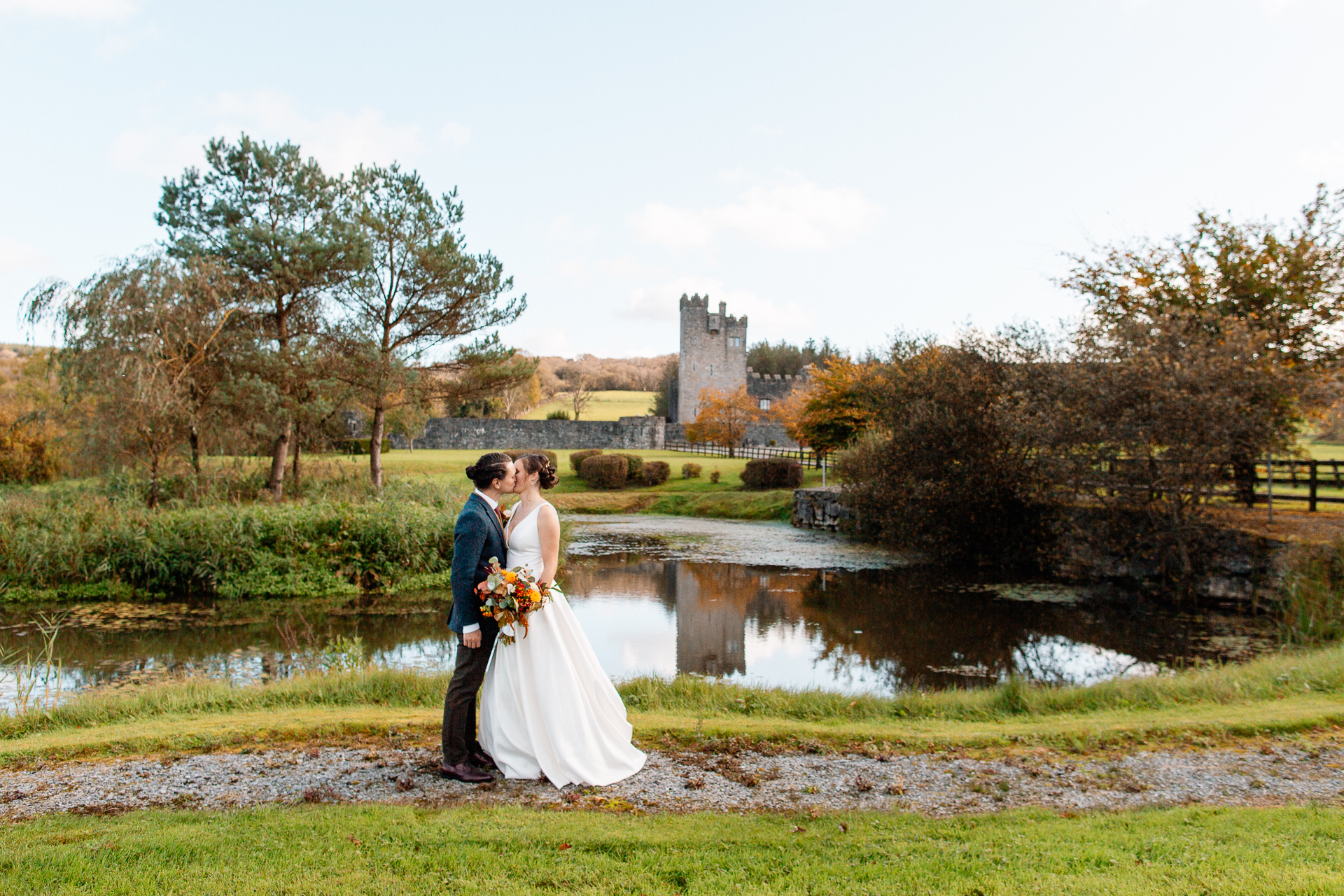 A man and woman kissing by a pond with a castle in the background