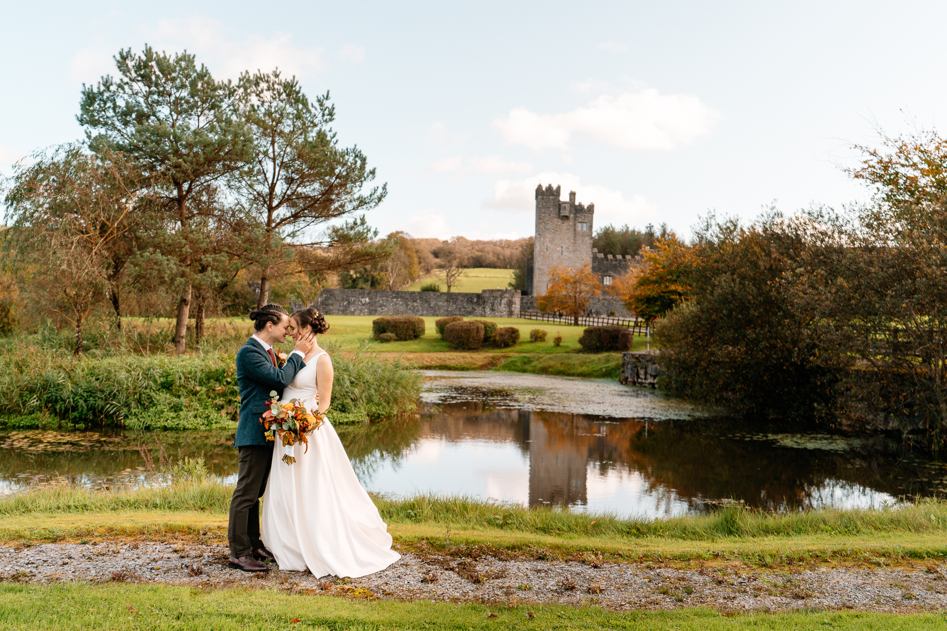 A man and woman kissing by a pond with a castle in the background