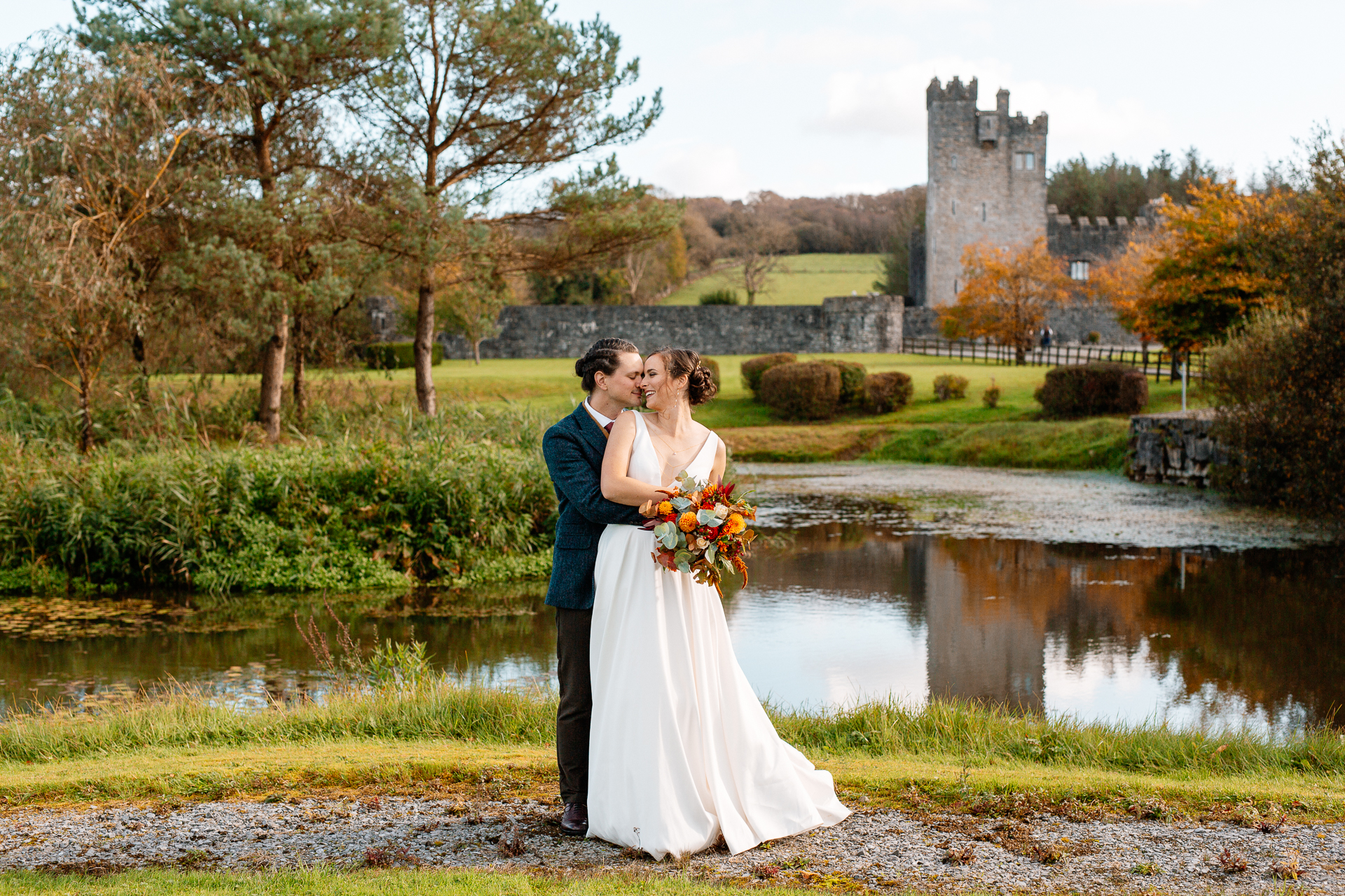 A man and woman kissing by a pond with a castle in the background