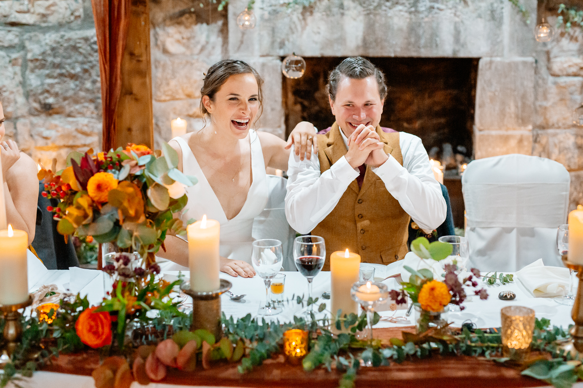 A bride and groom sitting at a table with flowers and candles