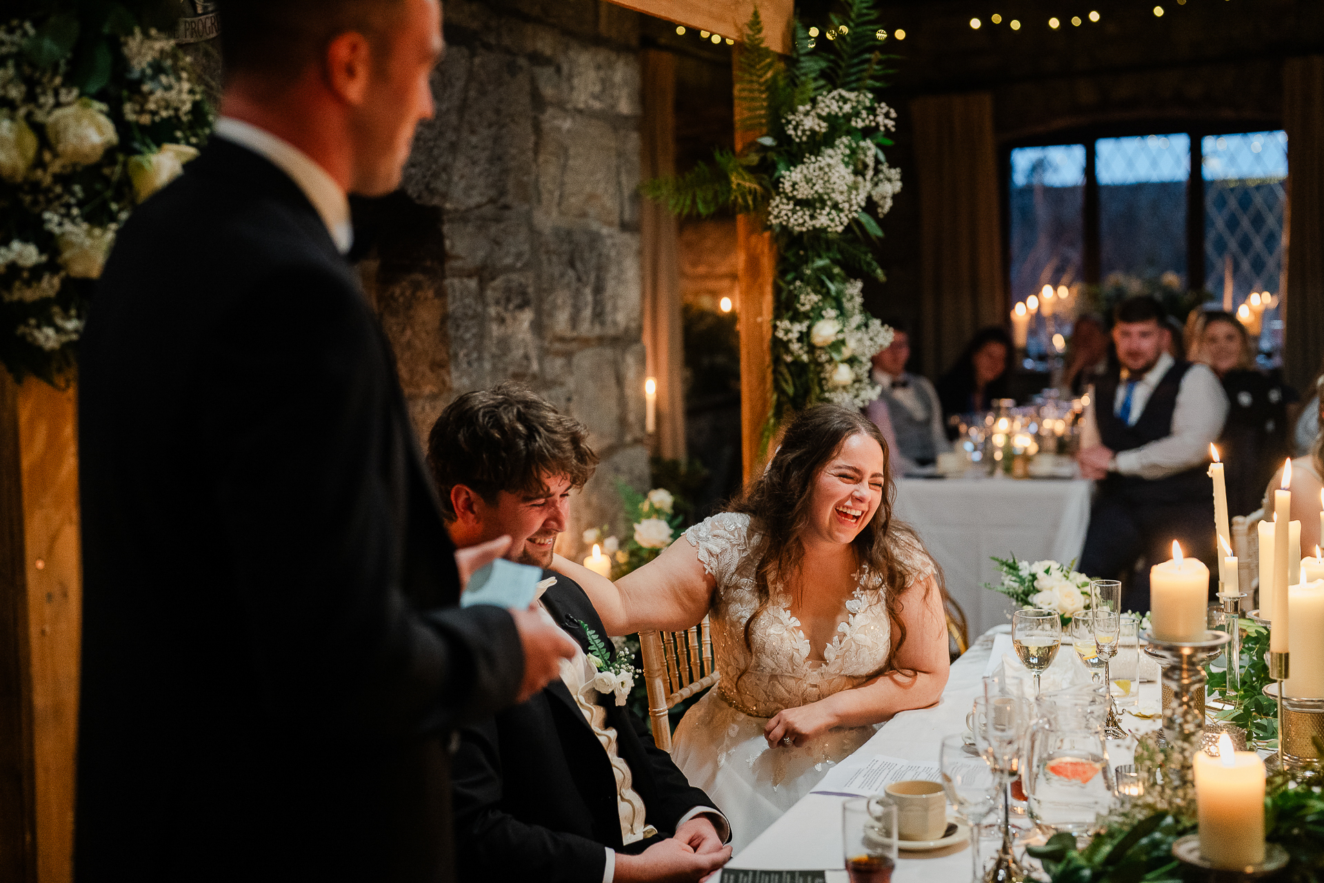 A man and woman sitting at a table with candles and flowers