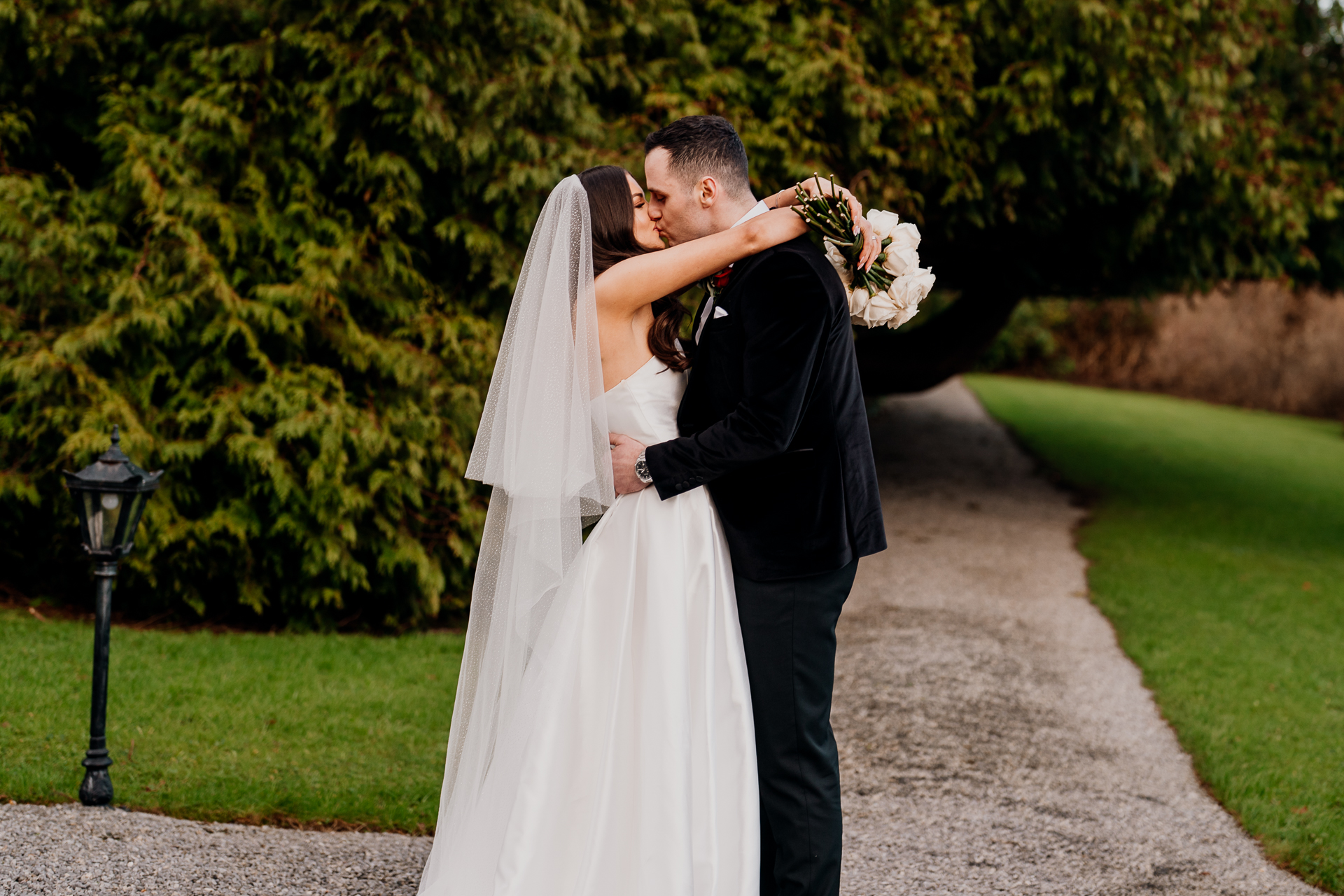 A man and woman kissing on a path in front of a hedge