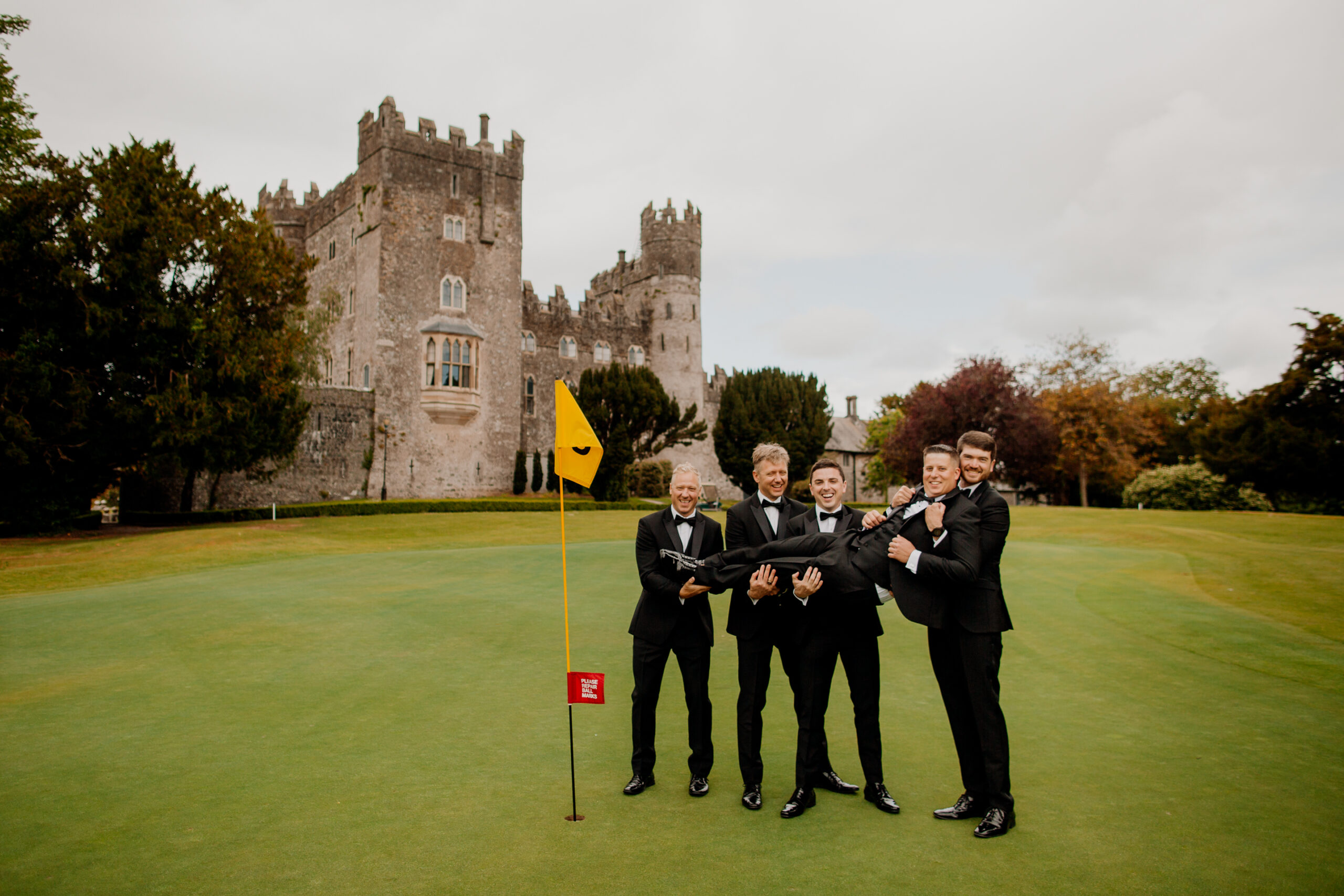 A group of men in suits standing on a golf course in front of a castle