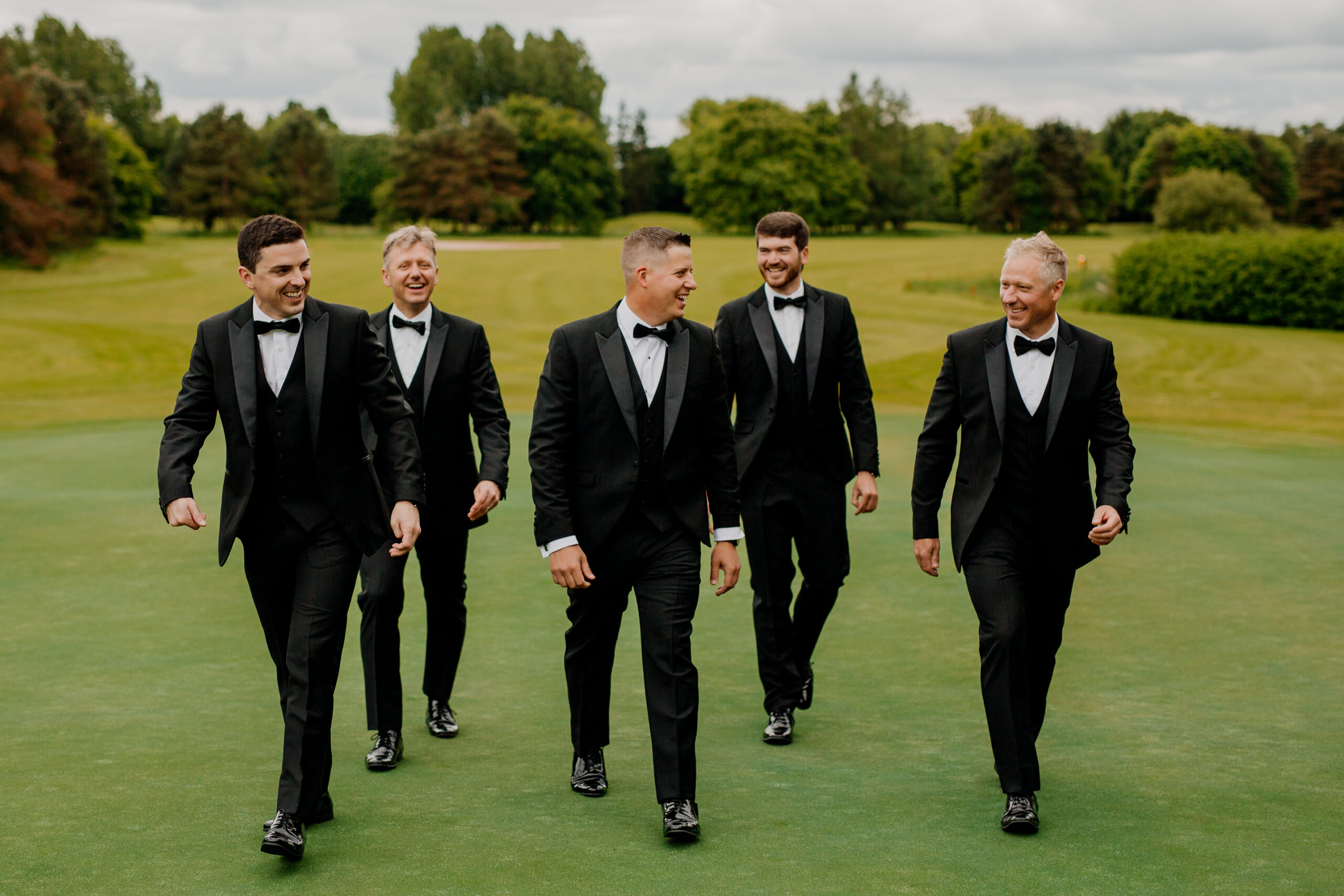 A group of men in tuxedos walking on a green field