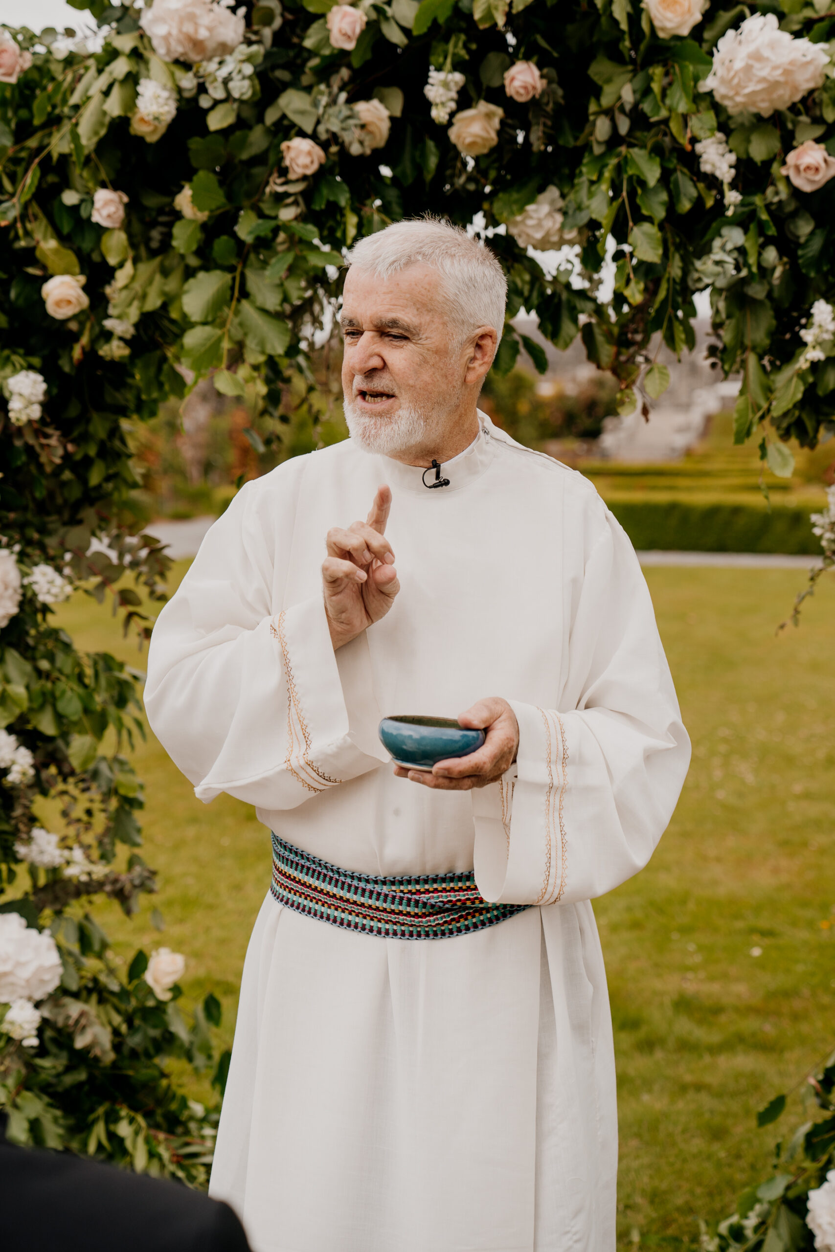 A man in a white robe holding a cup and a flowered tree