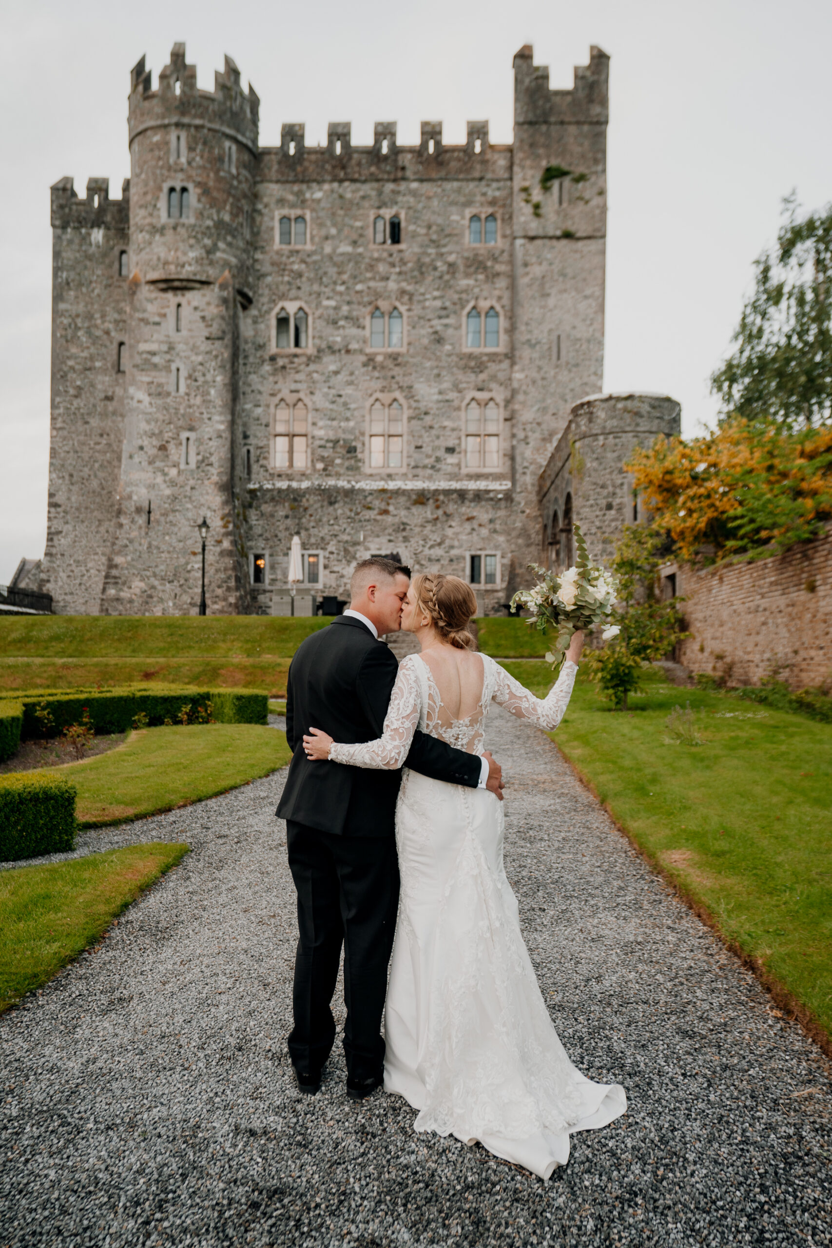 A man and woman in wedding attire kissing in front of a castle