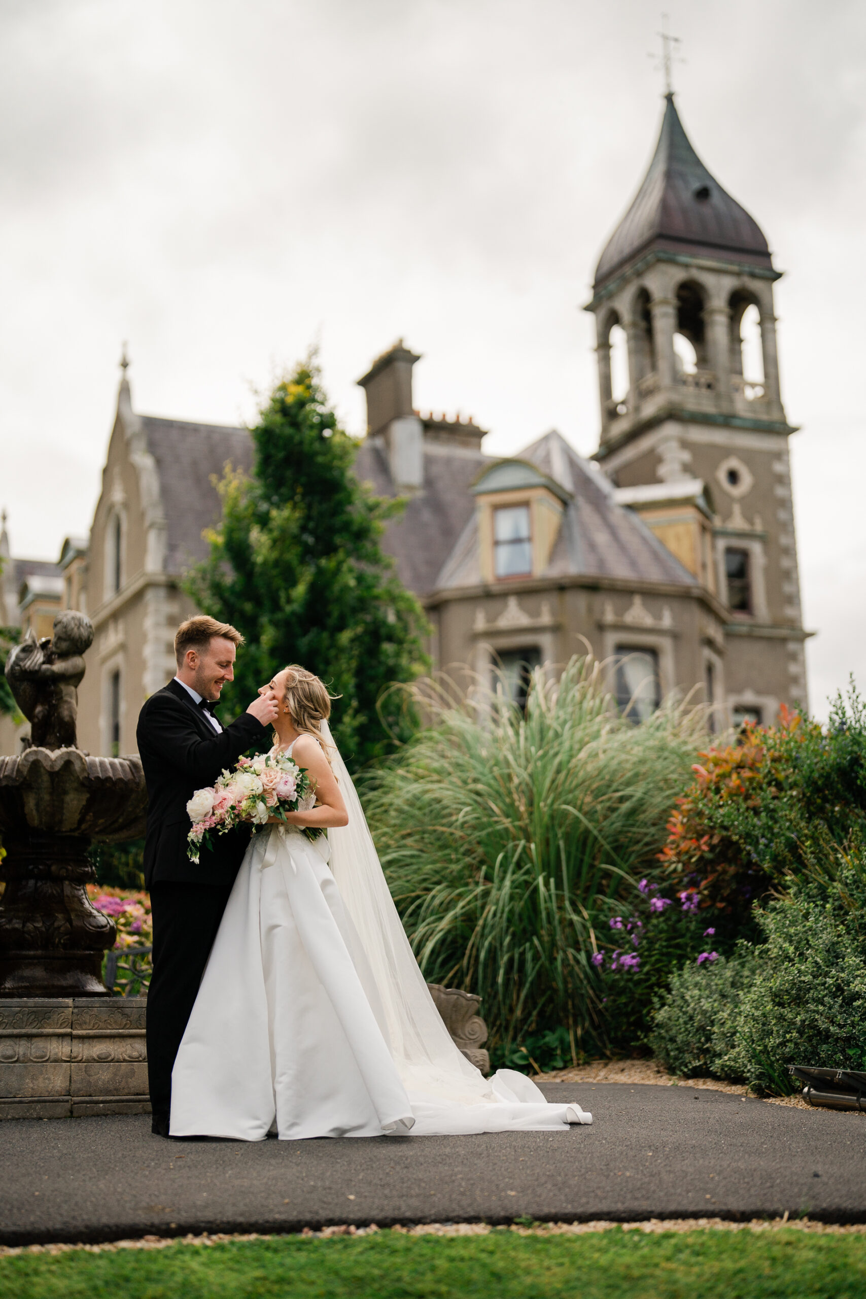 A man and woman in wedding attire kissing in front of a castle