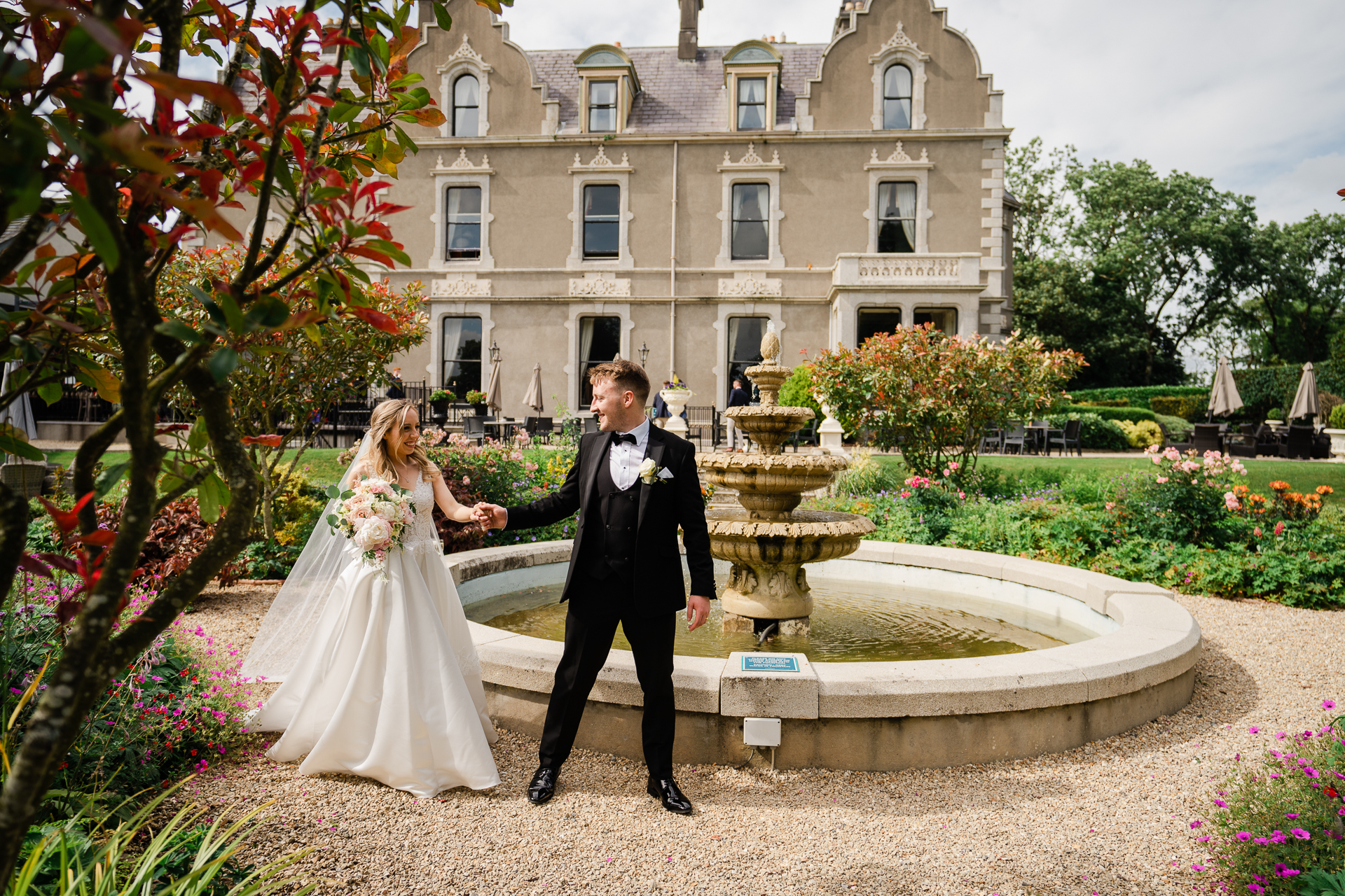 A man and woman in wedding attire walking down a path in front of a building