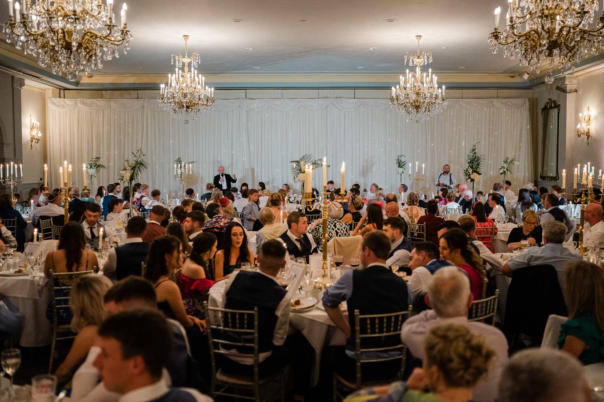 A large group of people sitting in a room with chandeliers