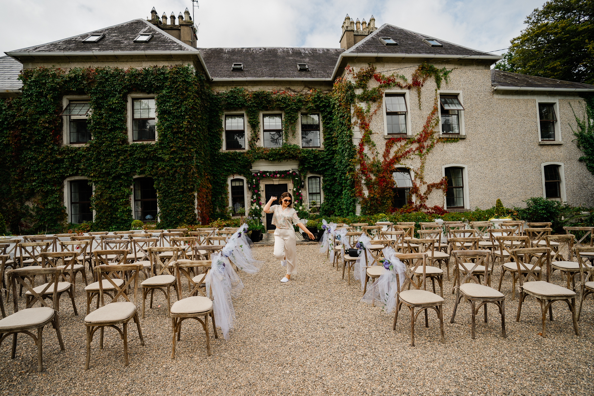 A person in a white dress walking through a courtyard with a row of chairs and tables and a