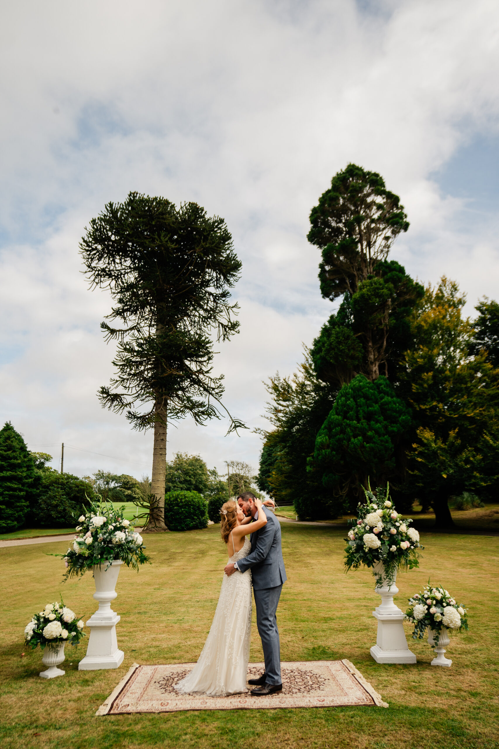 A man and woman kissing in a park with flowers and trees