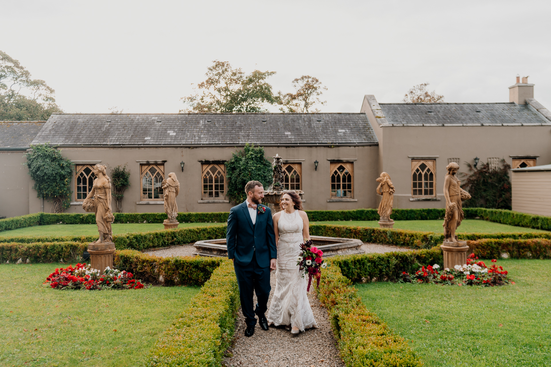 A man and woman posing in front of a house with statues