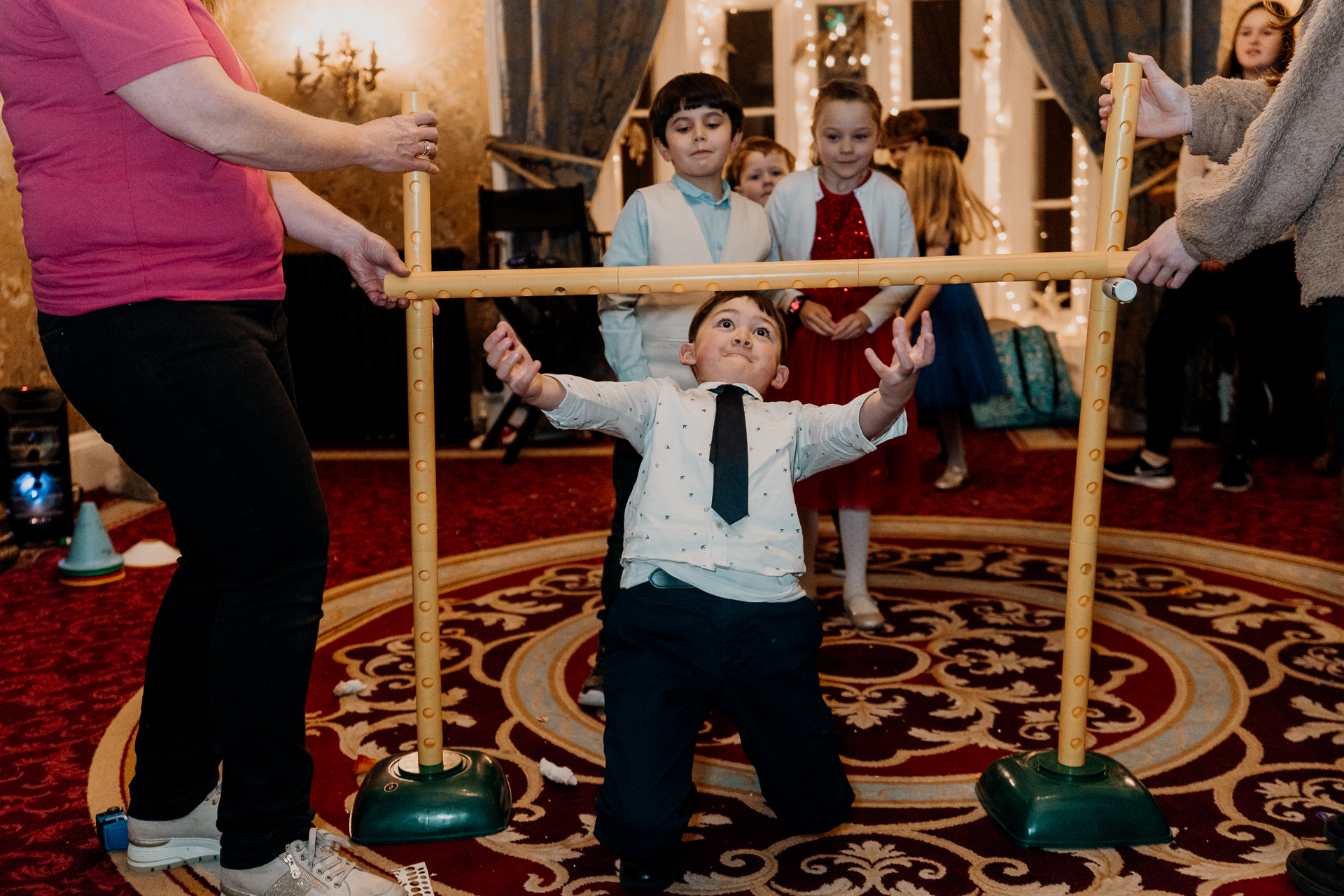 A boy in a suit and tie holding a stick in a room with other people