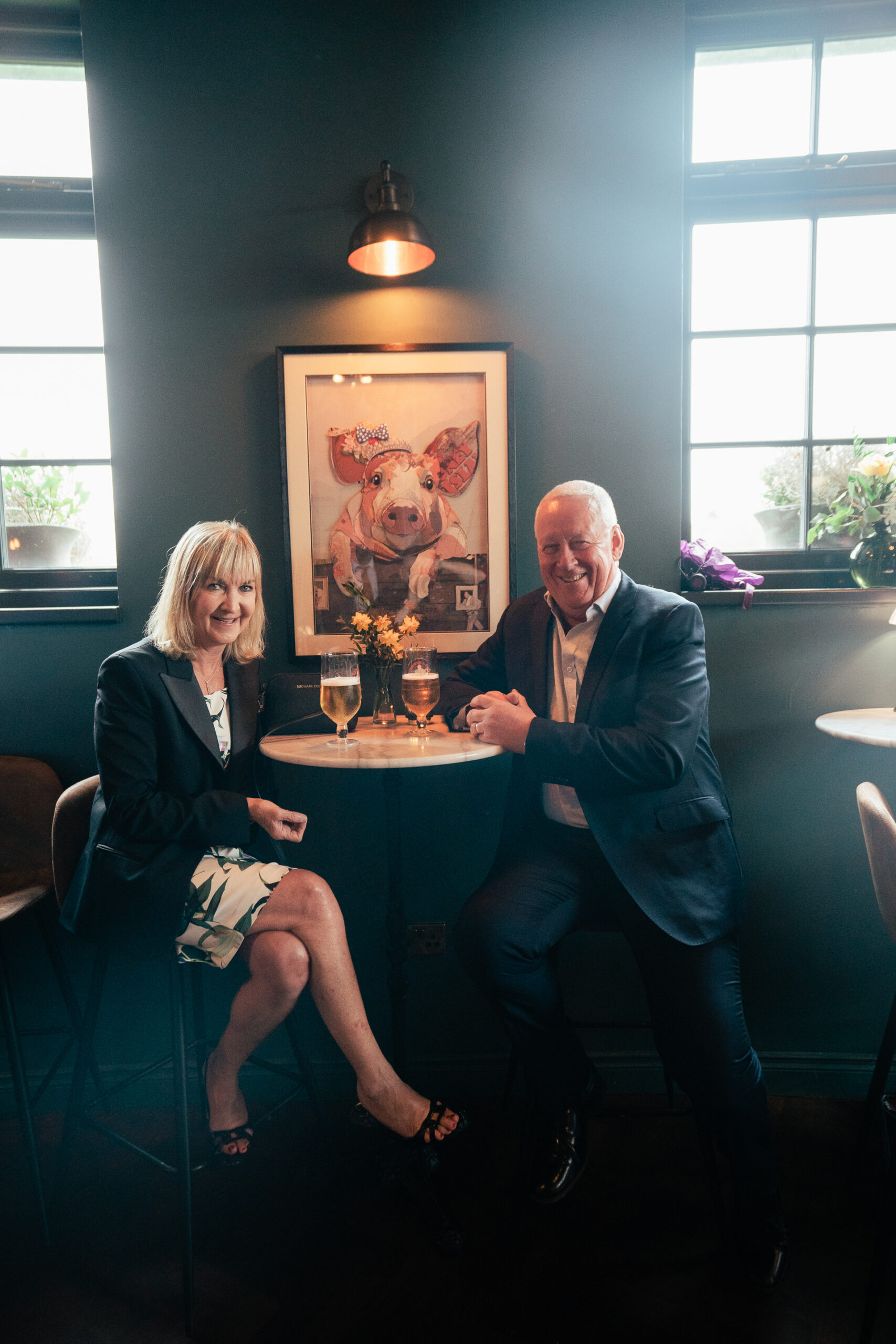 A man and woman sitting at a table with a painting on the wall