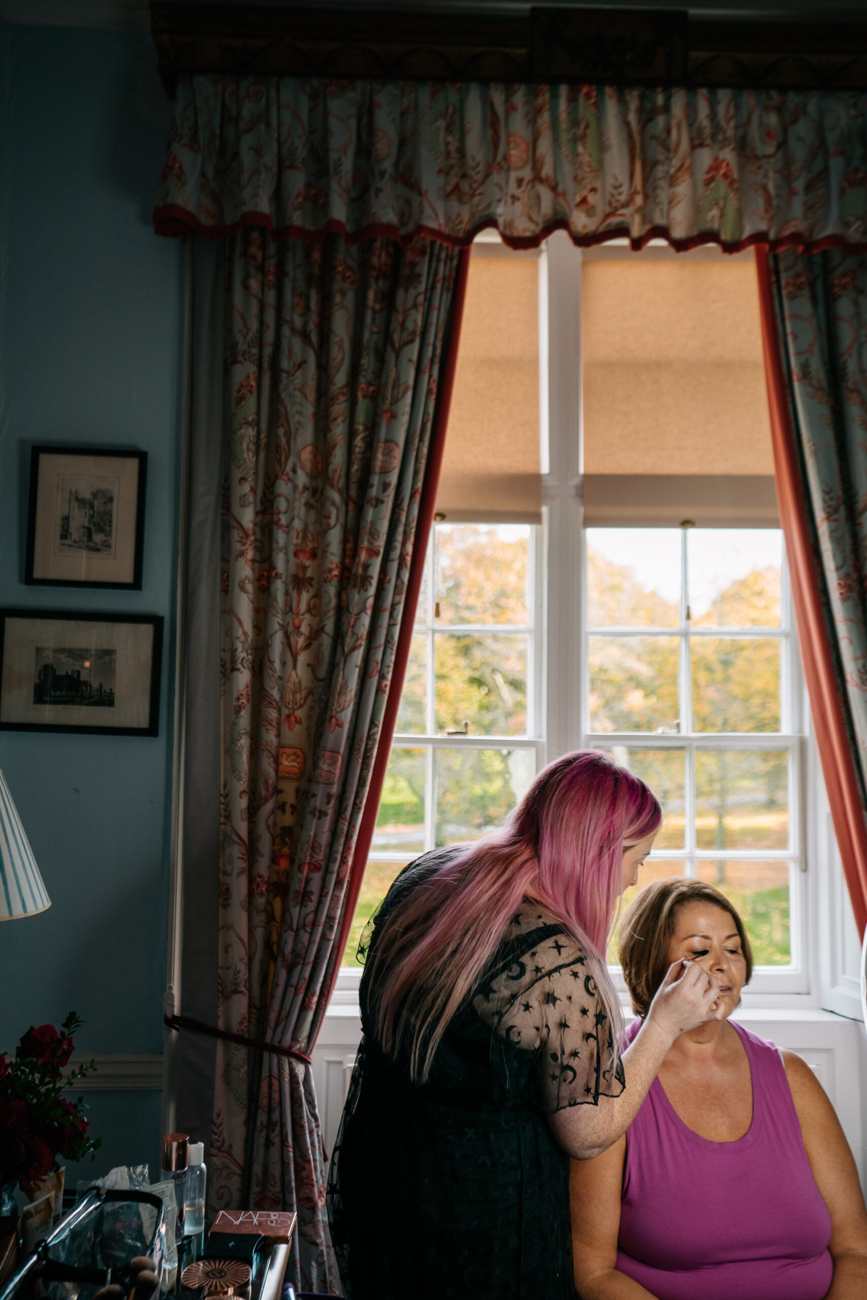 A woman with pink hair standing next to a woman with her hand on her face