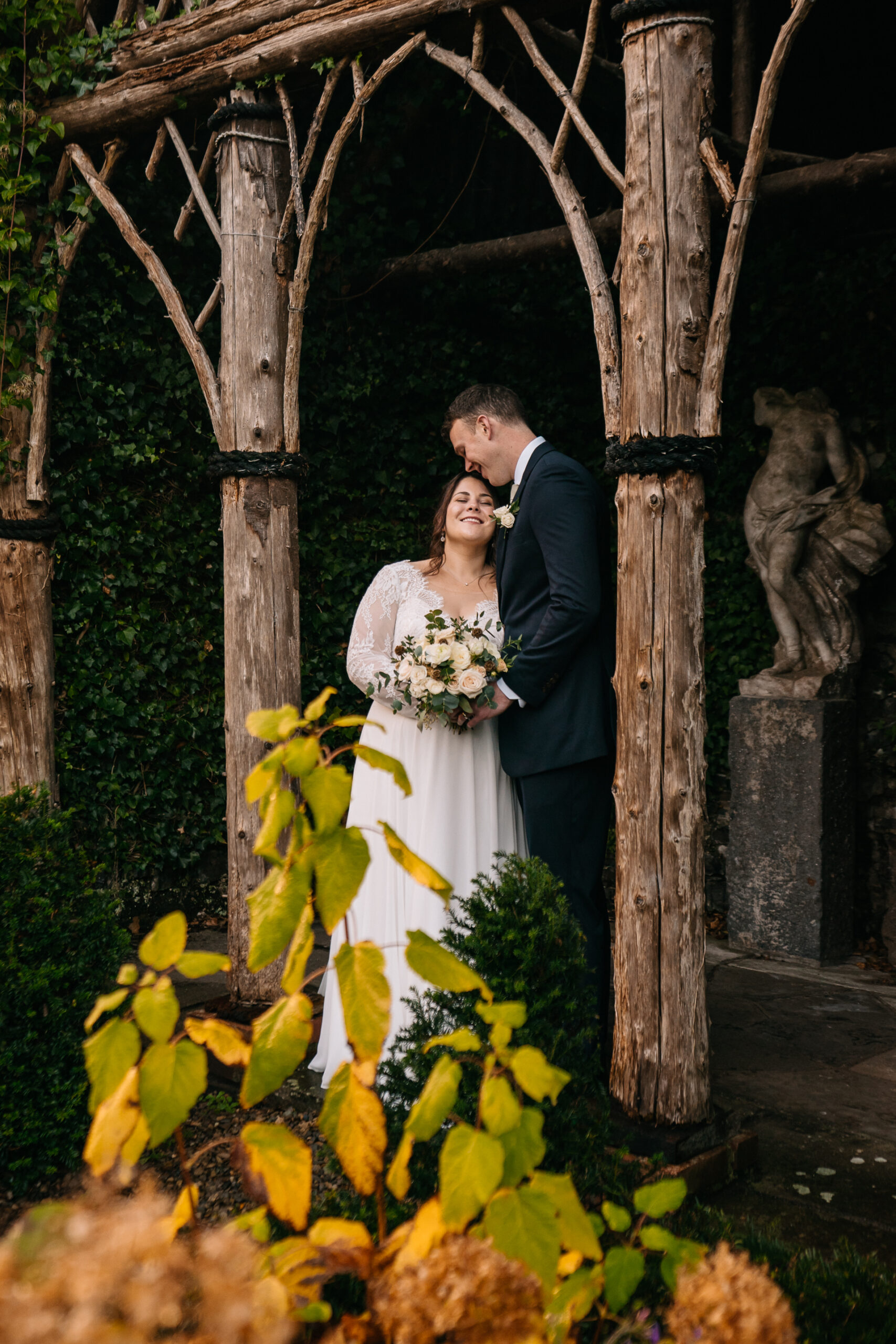 A man and woman in wedding attire standing under a tree