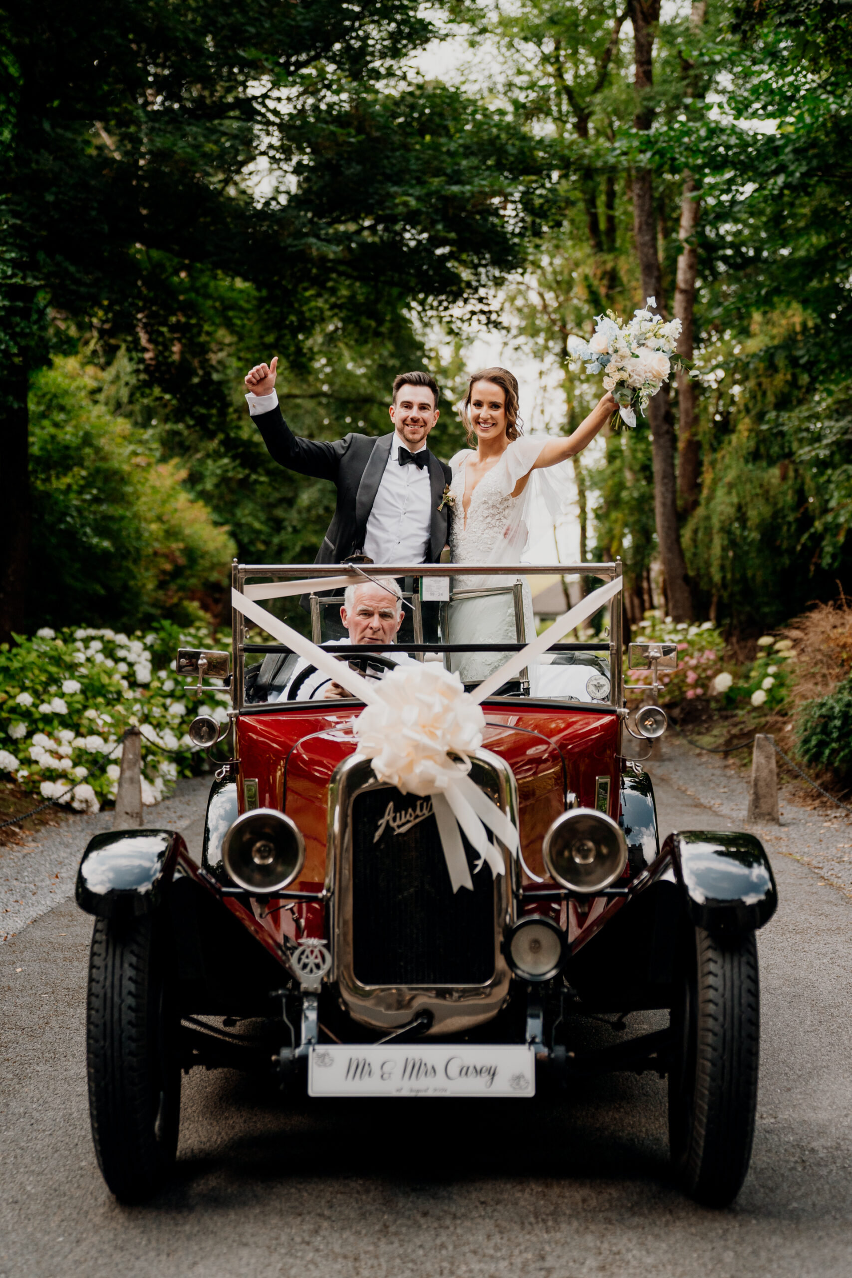 A man and woman in a convertible car with a bride and groom in the driver's seat