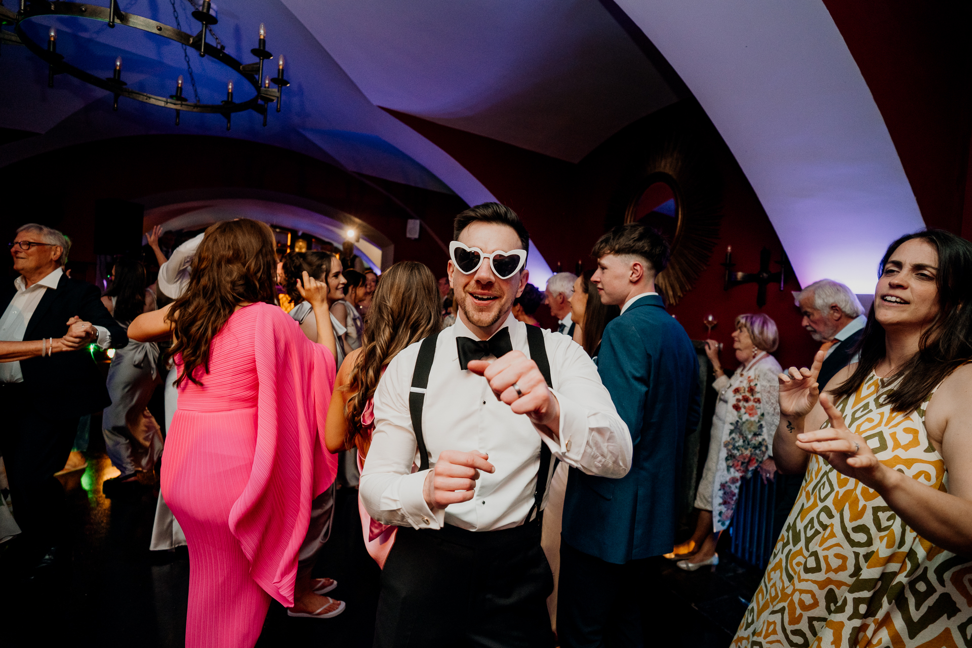 A person wearing a bow tie and sunglasses with a crowd of people around him