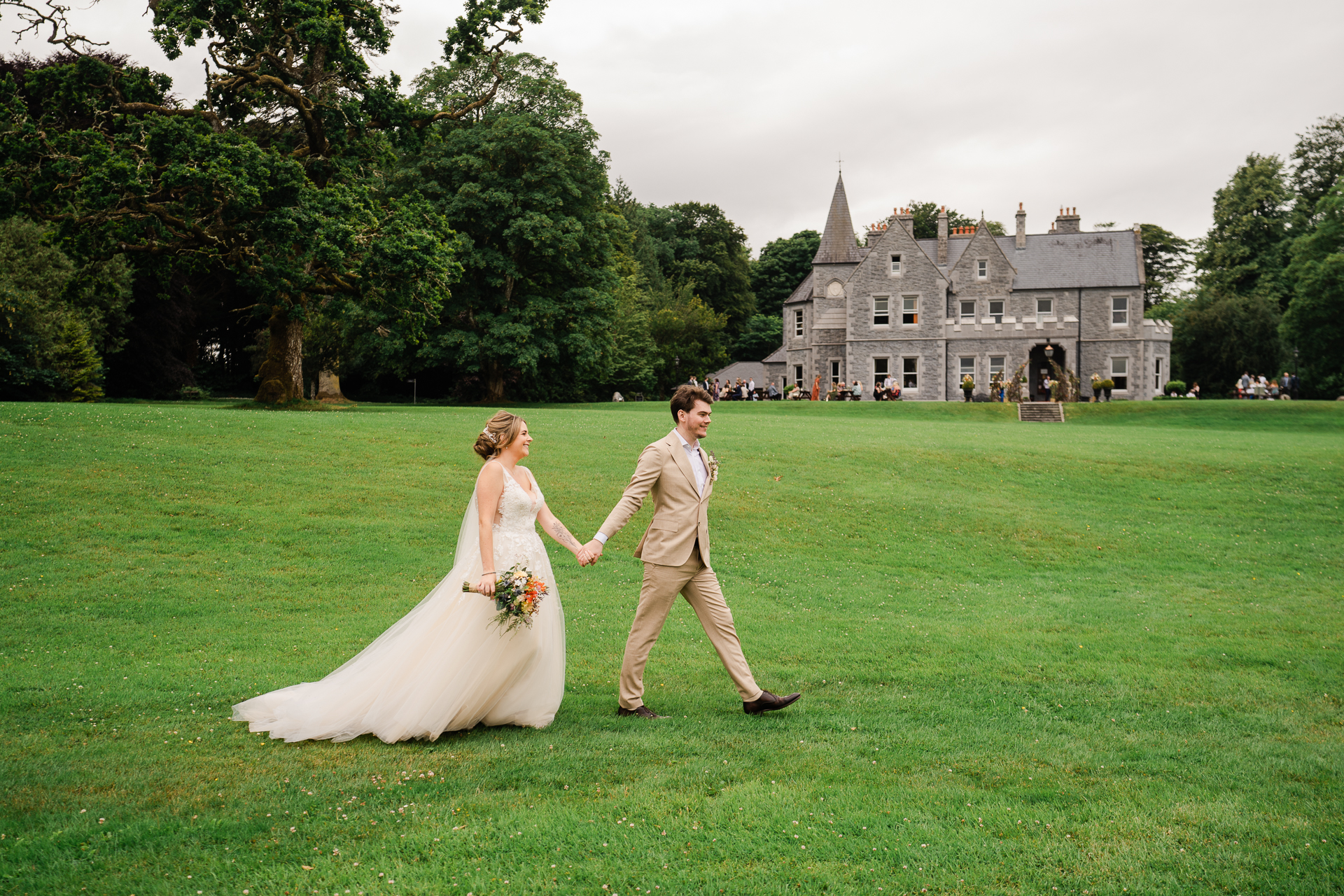 A man and woman walking in a grass field with a castle in the background