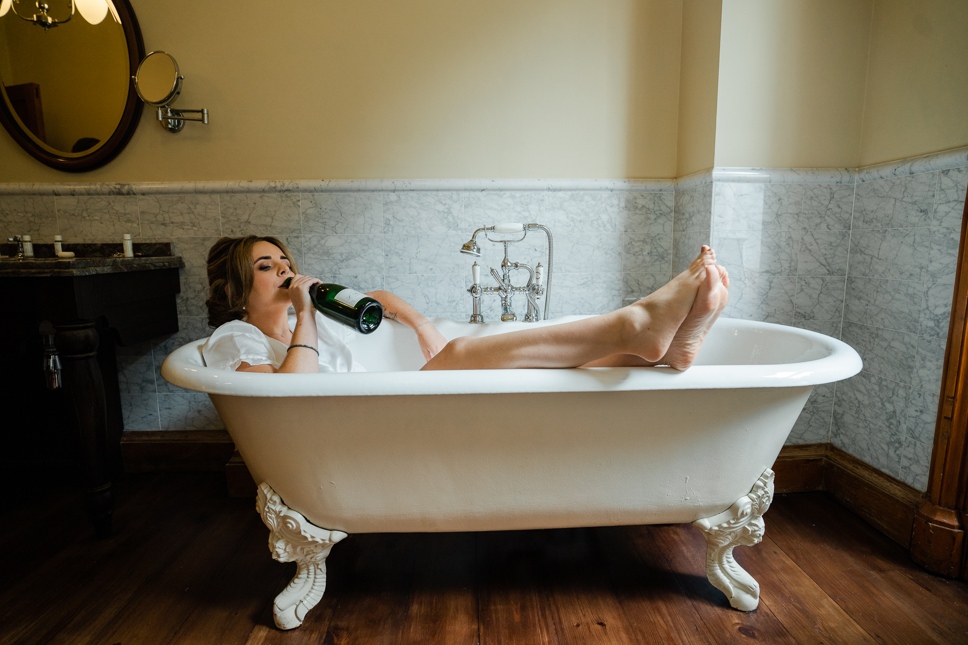 A person laying in a bathtub drinking a bottle of wine