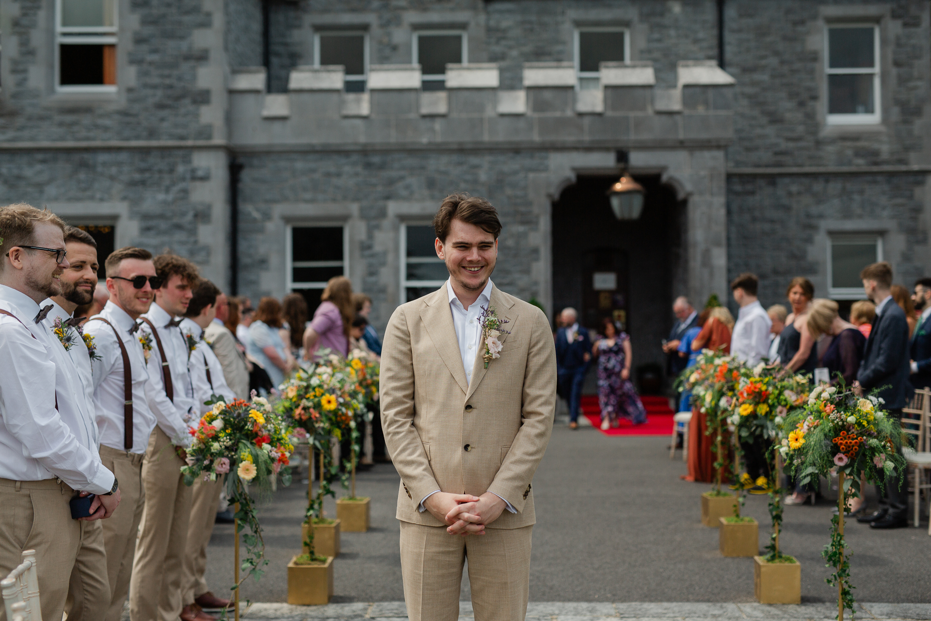 A man in a suit standing in front of a building with flowers