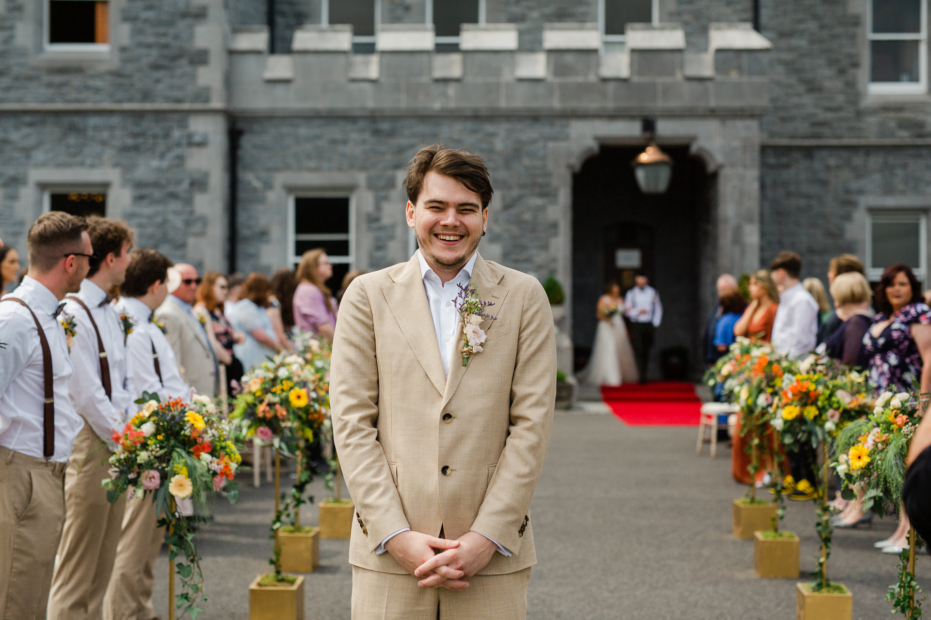 A man in a suit standing in front of a building with flowers