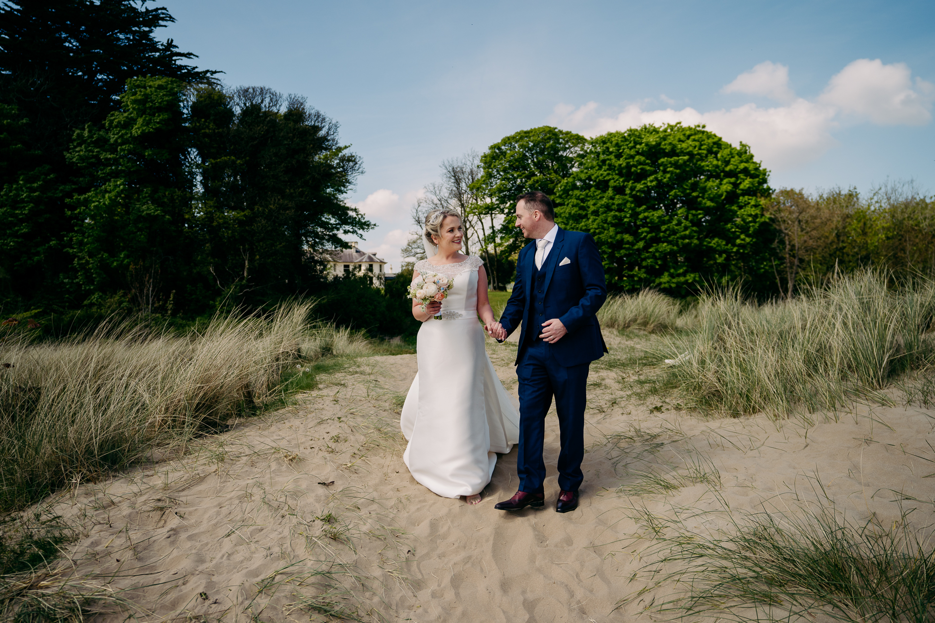 A man and woman walking on a dirt path with trees and grass