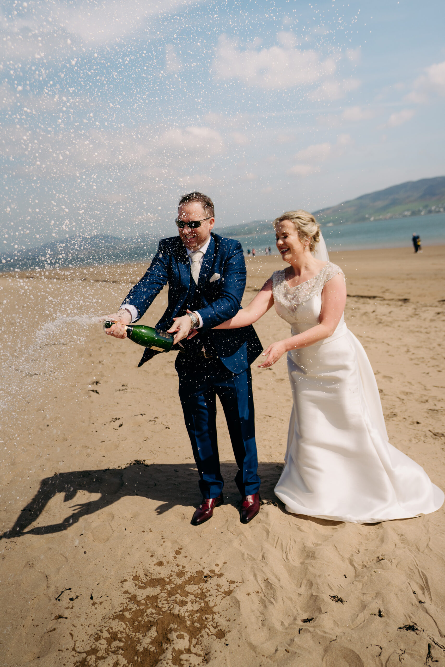 A man and woman holding a bottle and walking on a beach