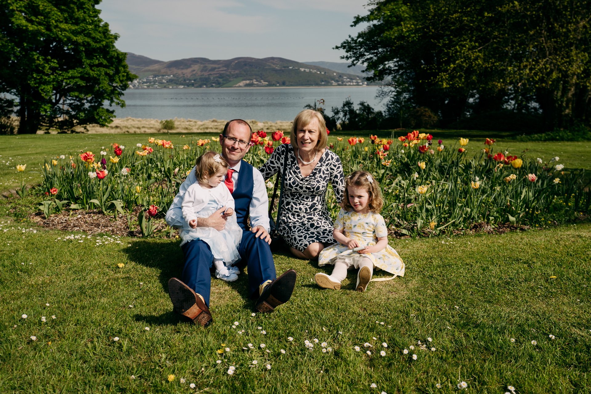 A person and two children sitting on grass by a body of water