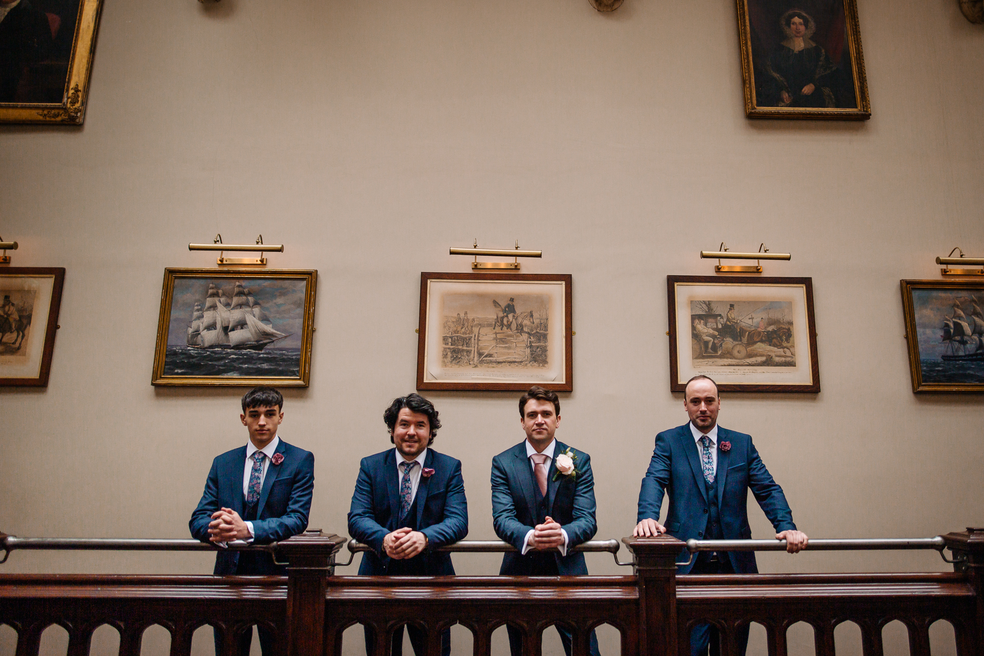 A group of men in blue uniforms sitting at a table with a wall of paintings