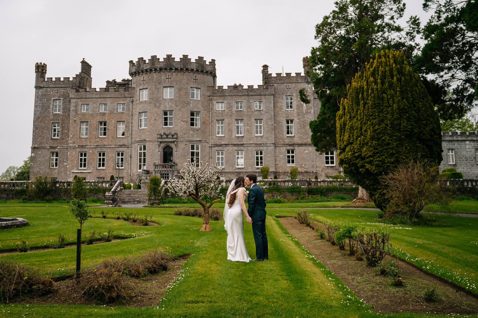 A man and woman in wedding attire kissing in front of a large building