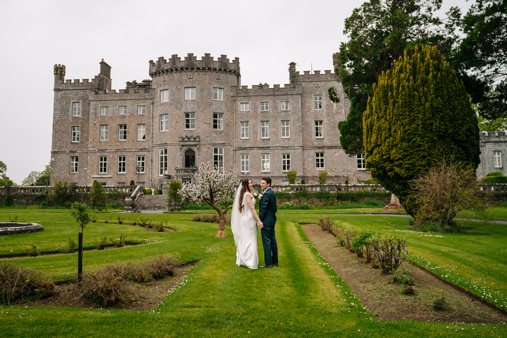 A man and woman in wedding attire kissing in front of a large building