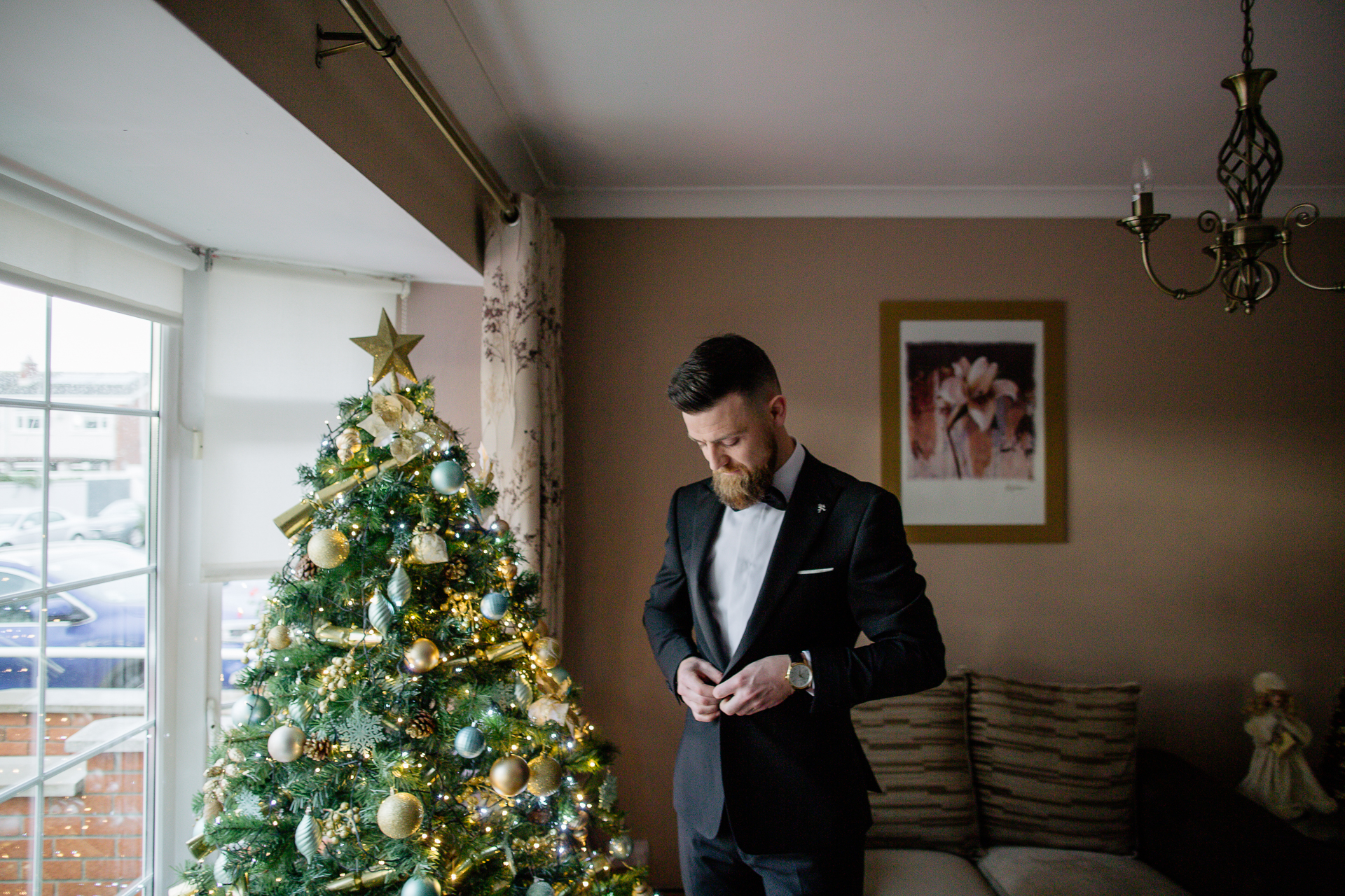 A person in a suit standing next to a christmas tree