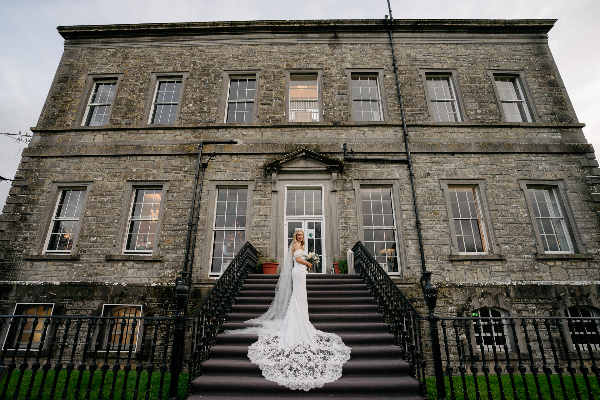 A person in a wedding dress on stairs in front of a large brick building