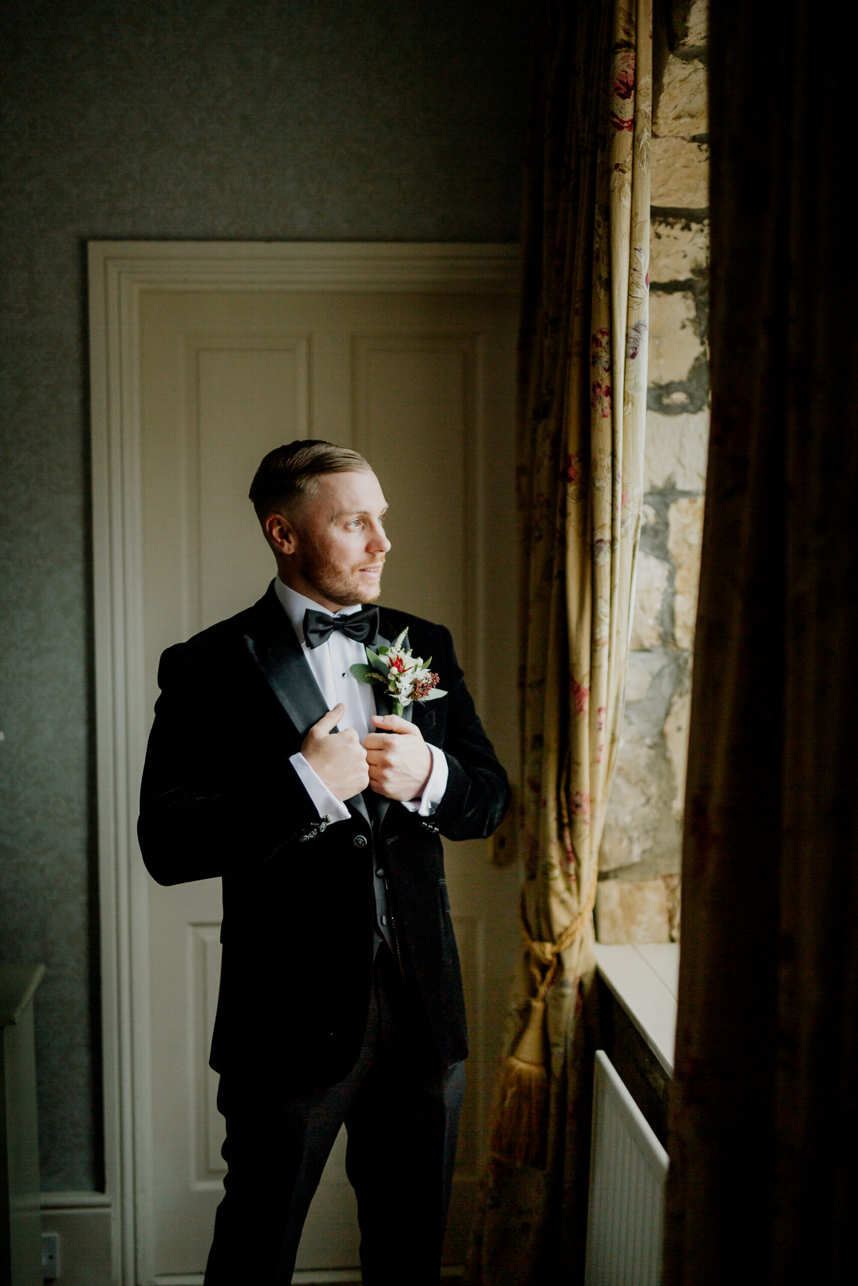 A man in a tuxedo holding flowers in a doorway