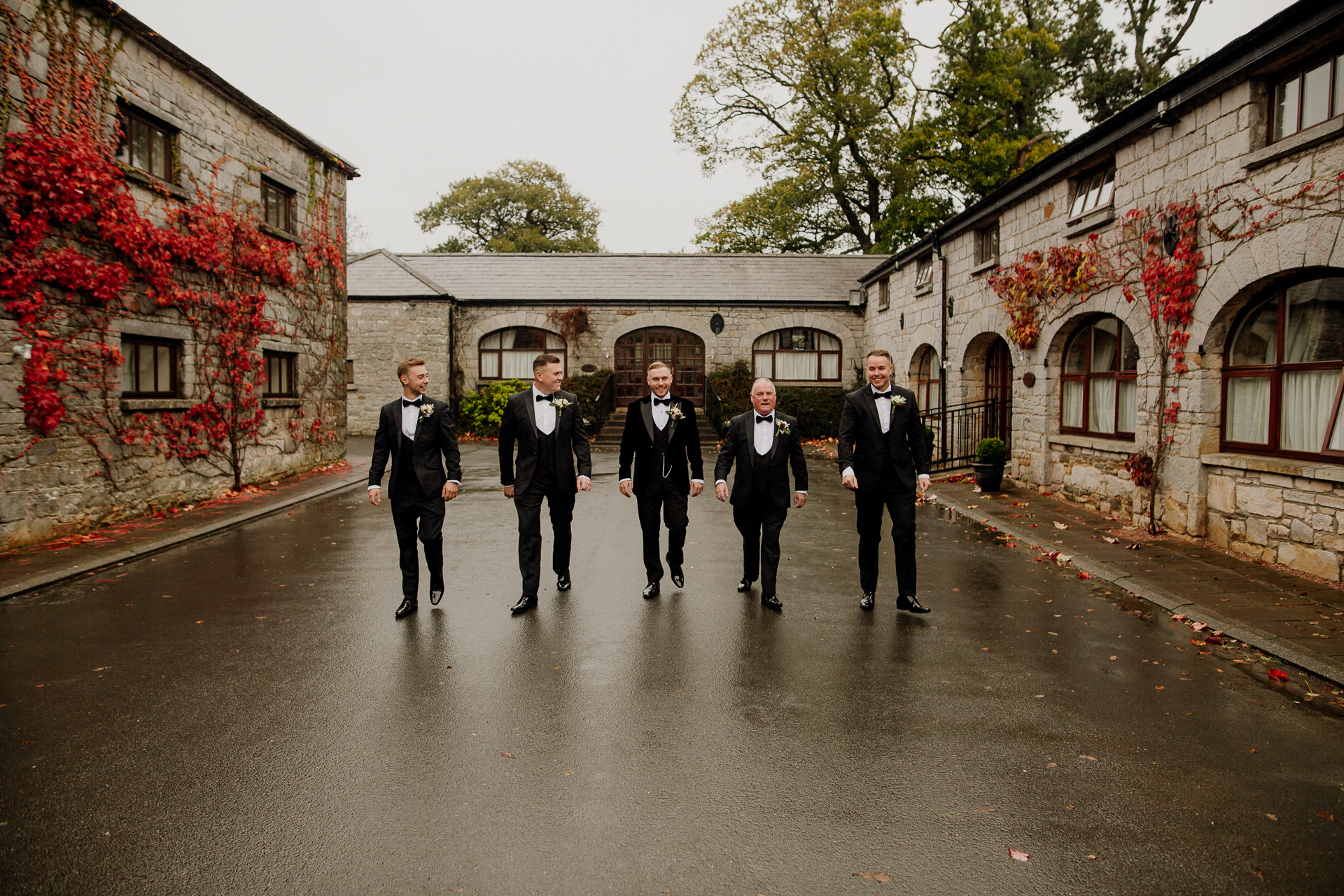 A group of men in black suits walking down a wet street