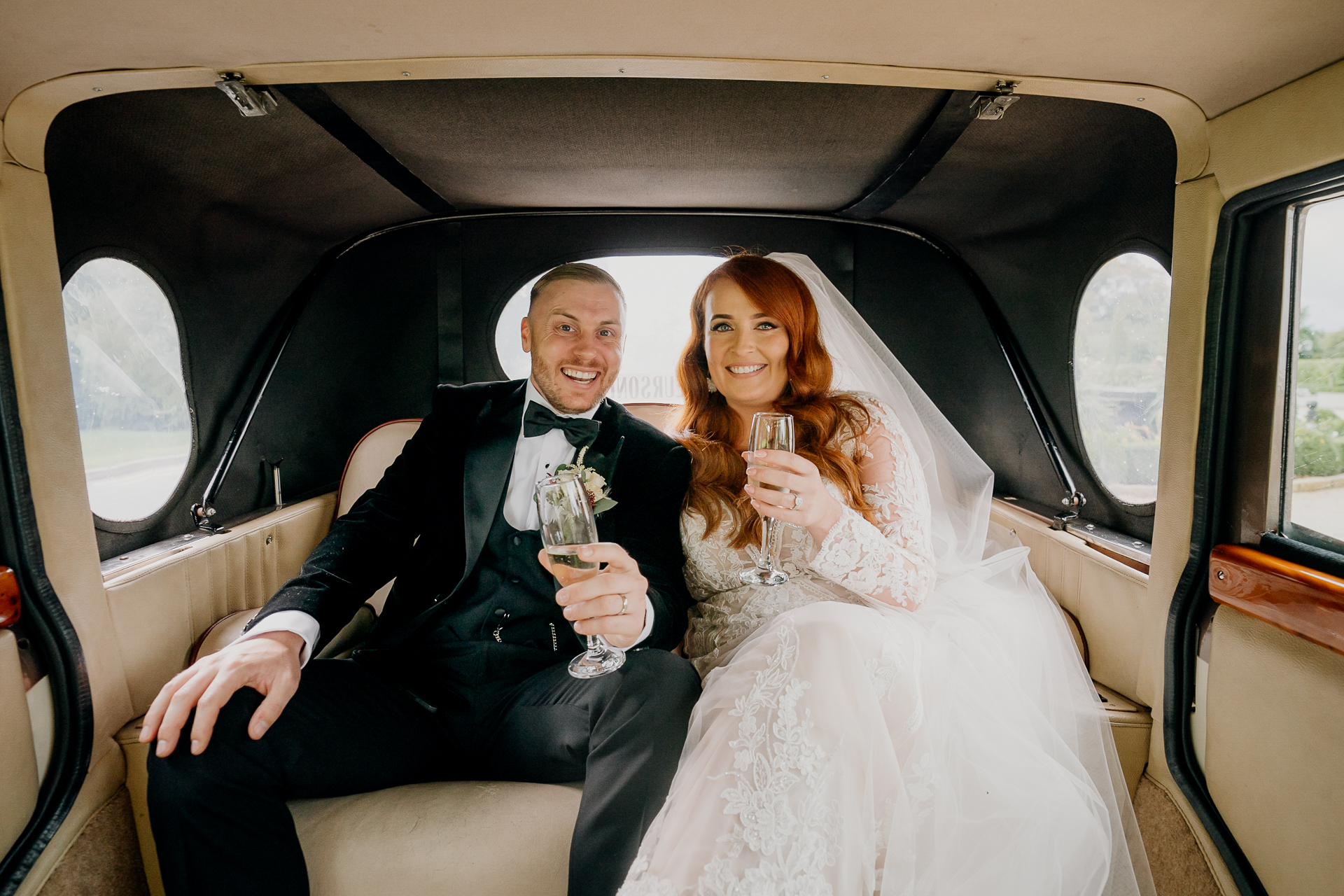 A man and woman sitting in a car and holding wine glasses