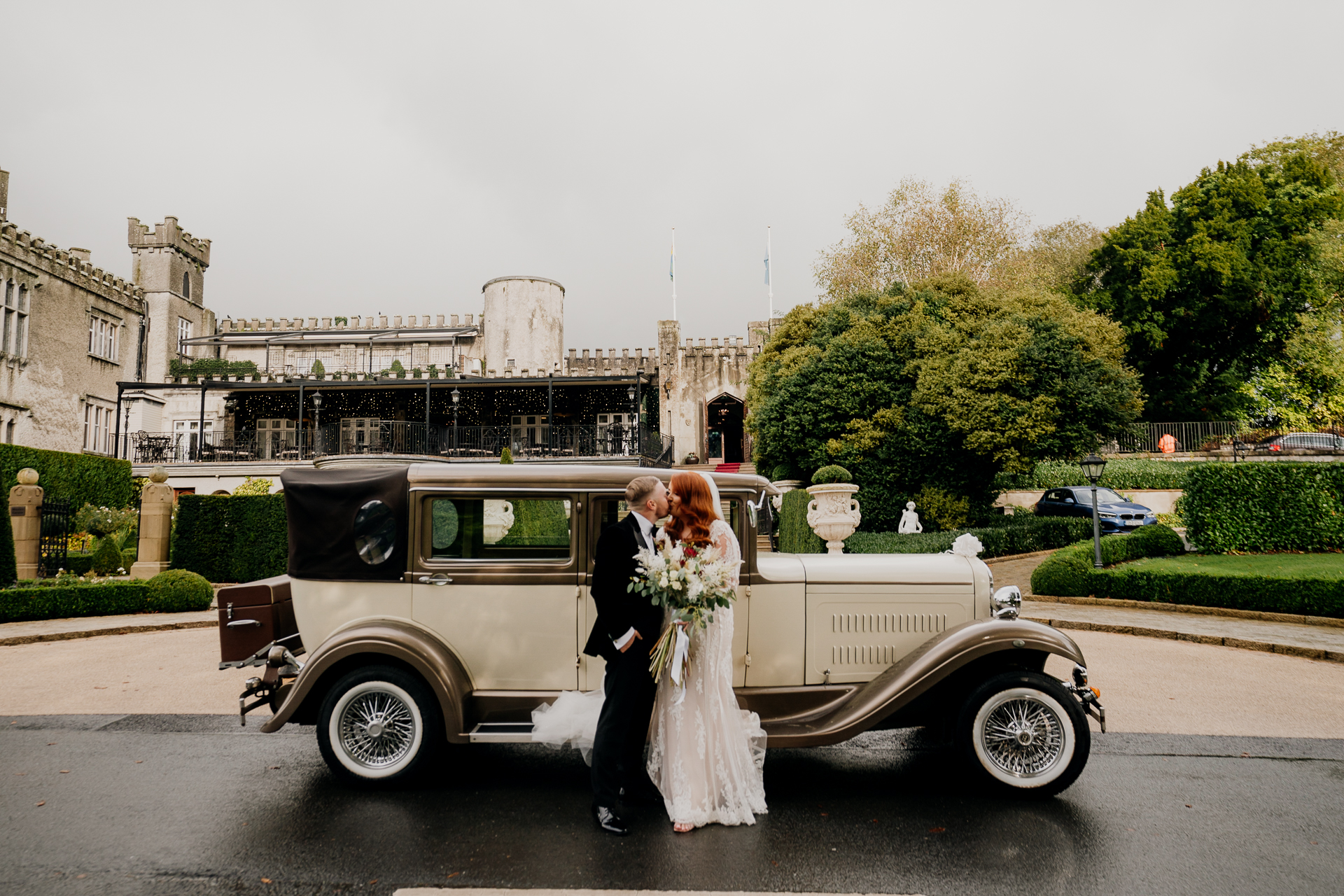 A man and woman in wedding attire standing in front of a car