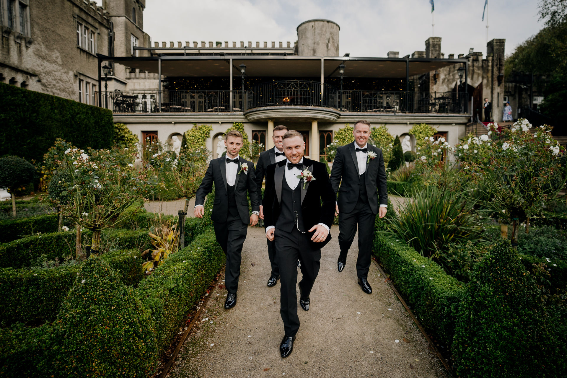 A group of men in suits walking down a path in front of a building with many plants