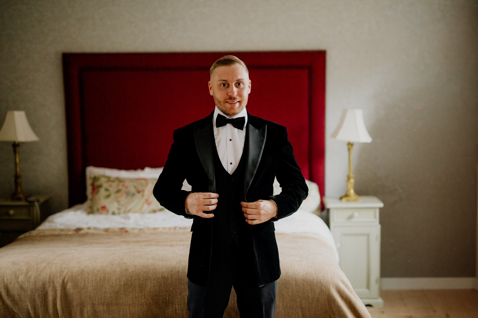 A man in a tuxedo standing in front of a bed