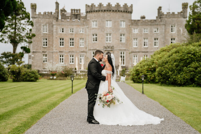 A man and woman in wedding attire kissing in front of a large building