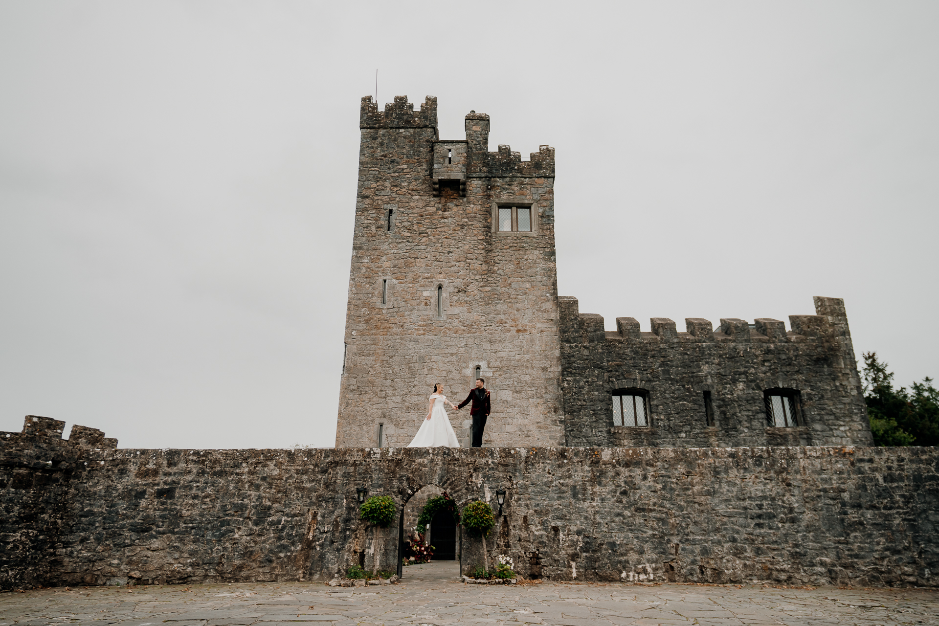 A bride and groom standing in front of a stone castle