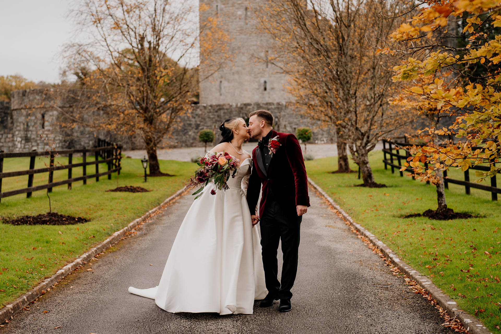 A man and woman kissing on a path with trees and grass