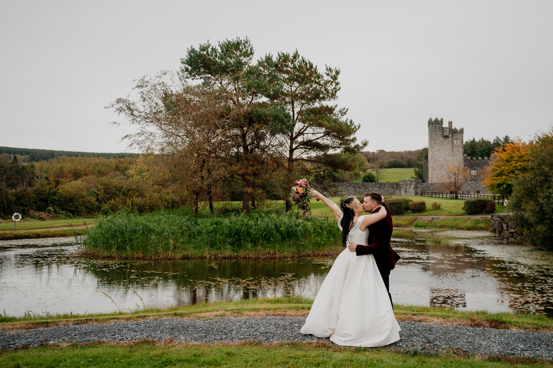 A man and woman kissing by a pond with a castle in the background