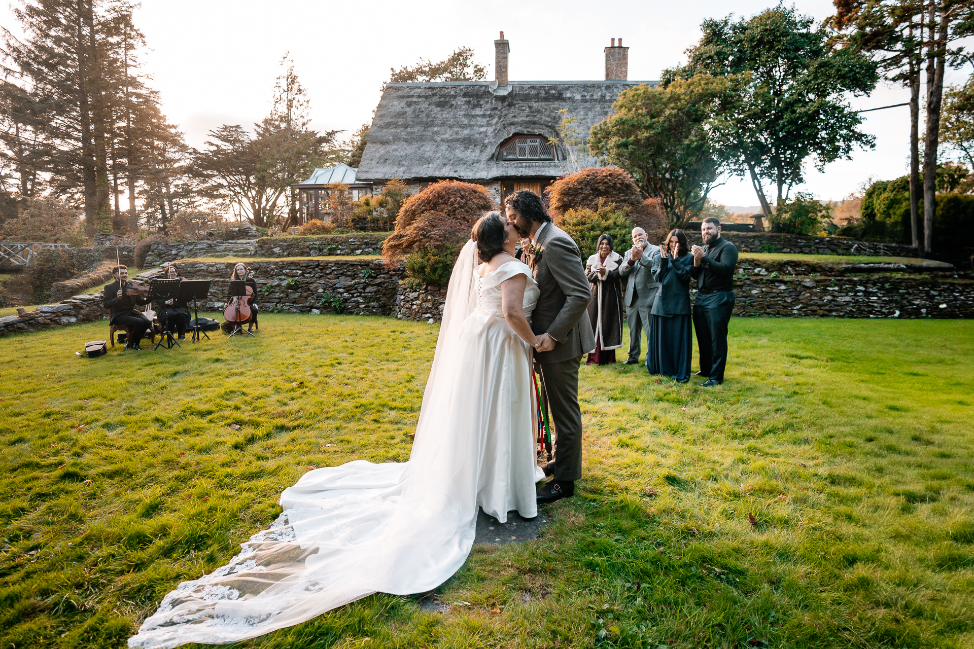 A man and woman kissing in a field with a house in the background