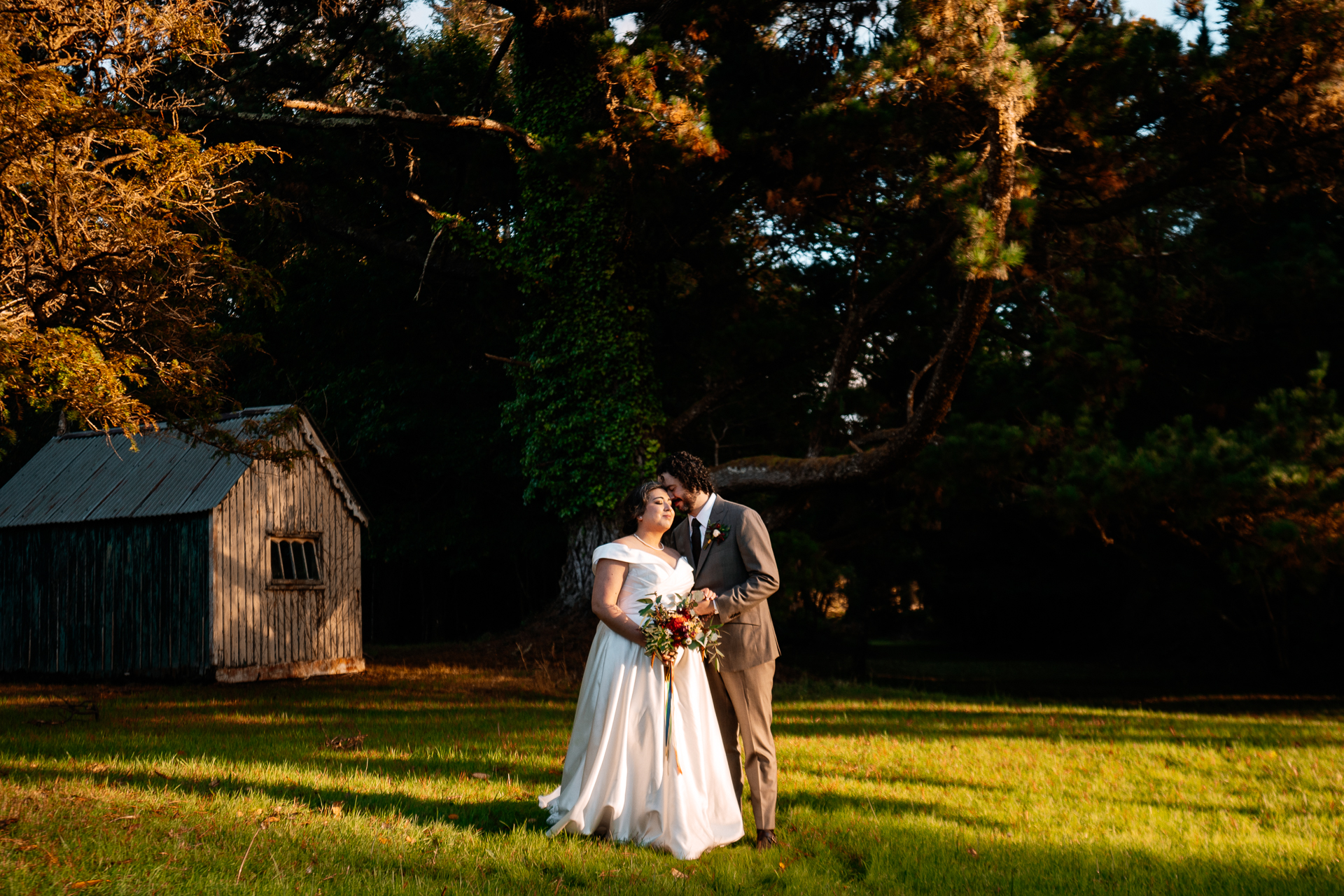 A man and woman kissing in a field with trees and a barn