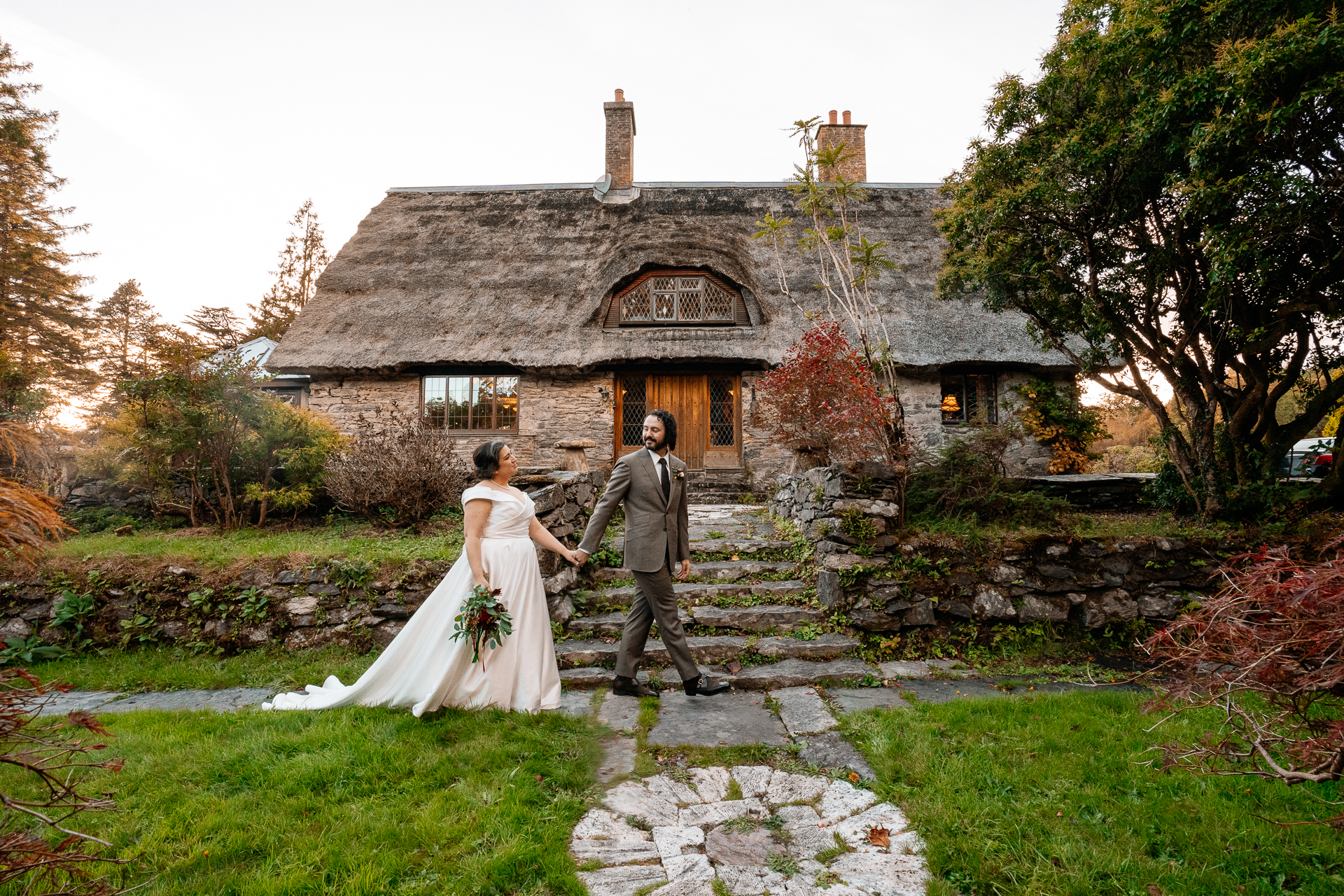 A bride and groom walking down a stone path in front of a house