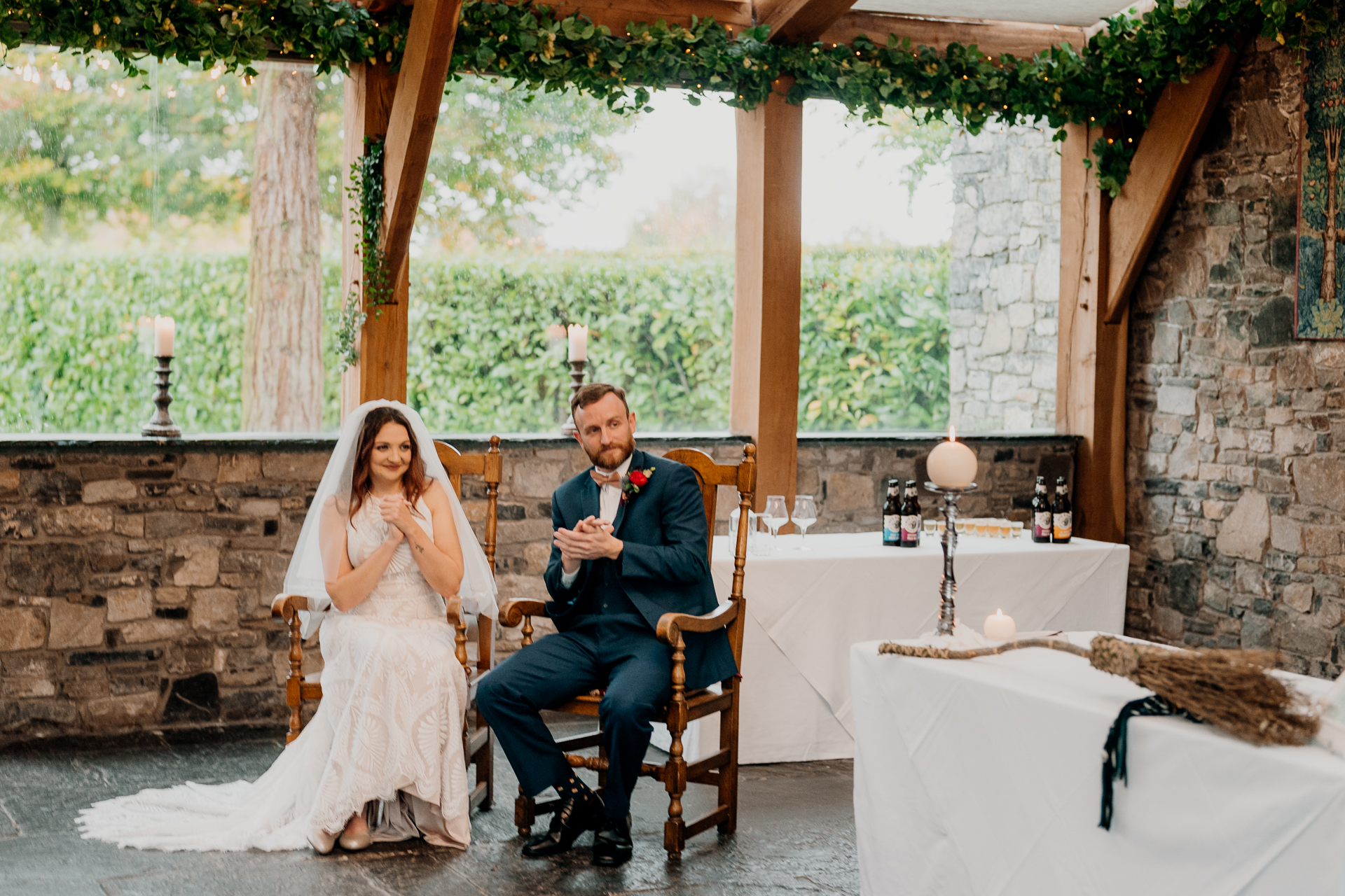 A bride and groom sitting in a chair in a room with a stone wall and a table with